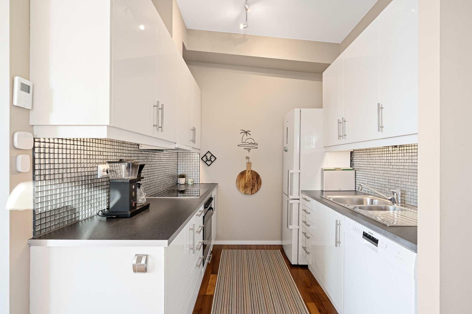 Kjøkkenet har godt med skap- og benkeplass, hvite fronter og pene mosaikkfliser over benk. Galleribilde