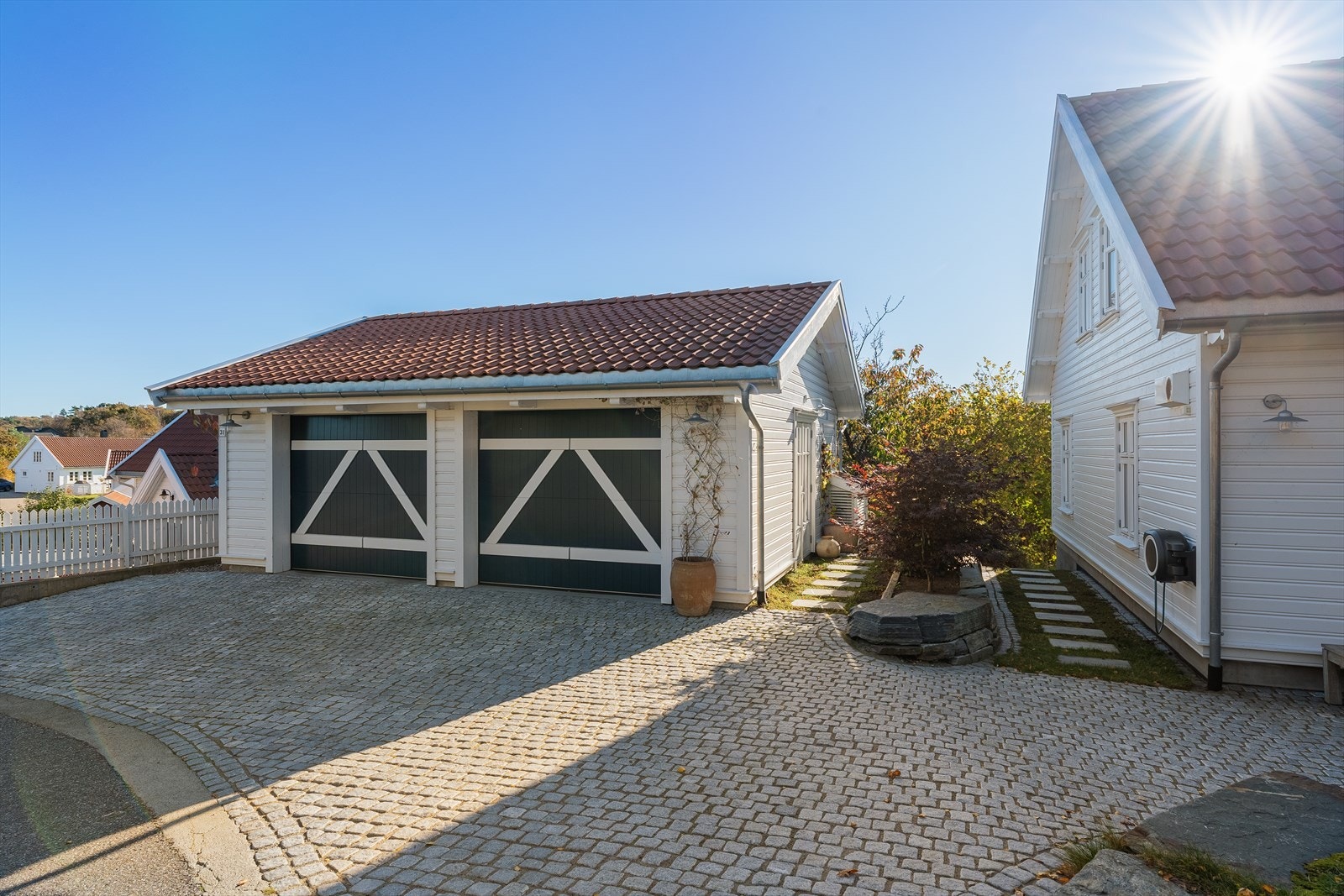 Mellom den doble garasjen er det laget til et flott plantebed med en nydelig japansk viftelønn, som får en flott blodrød farge. Det er også en vintergrønn hekk, samt plantet et japansk kirsebærtre blomstrer pent rosa i mai Galleribilde