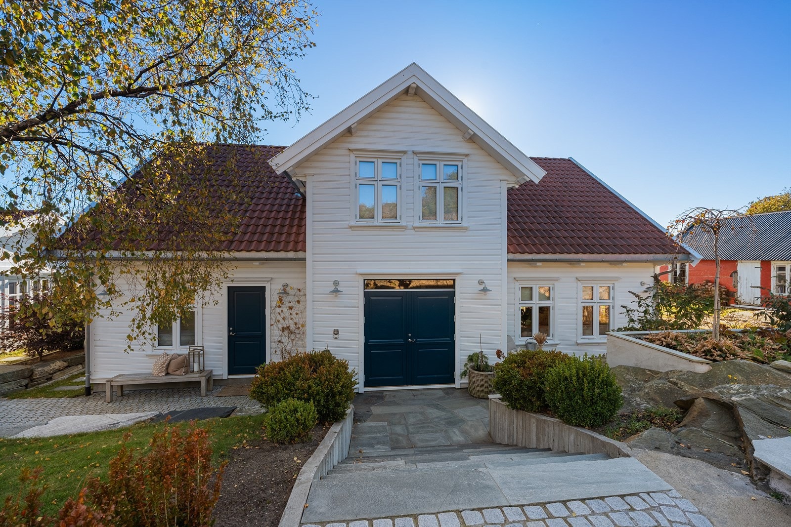 Inngangspartiet er vakkert opparbeidet med brostein, plantebed, skifer mm. Det er også laget til flere plantebed i terrenget med skiferheller og gangsti på fjellet. Mellom garasjen og boligen er det lagt skiferheller, samt plantet med sedum Galleribilde