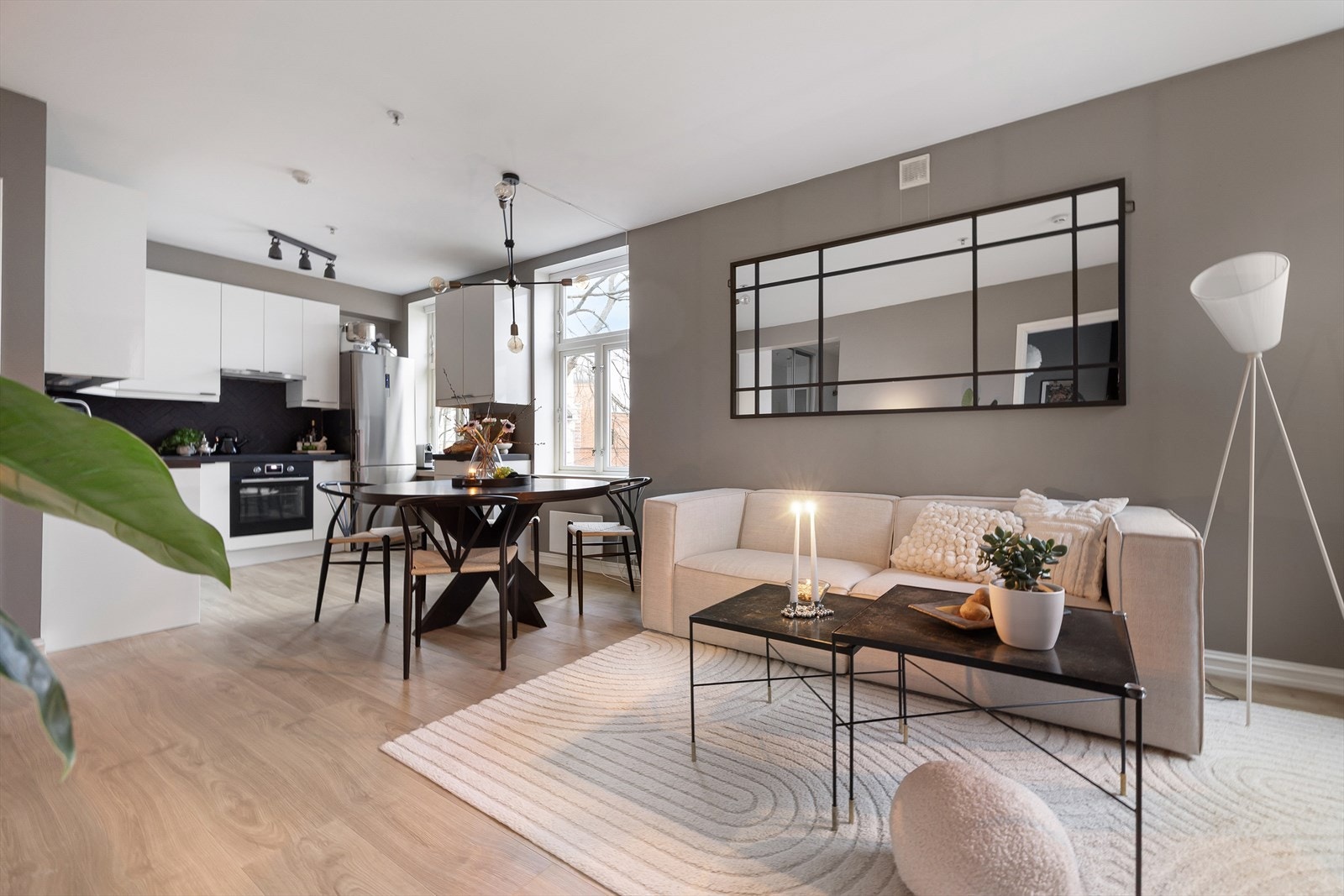 Vel inne i stuen, åpner rommet seg fint i en flate som kombinerer stue og kjøkken. Her finner du god plass til både spisestue og sofakrok. Veggene er slettmalte i en dempet gråfarge og møter det hvite taket listfritt _ et moderne grep. Galleribilde