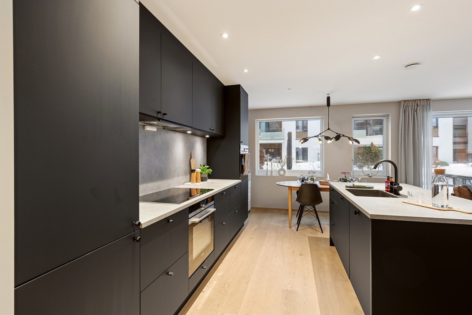 Kjøkkenet fra 2020 fremstår moderne og stilrent, med sorte, glatte fronter og lys benkeplate med nedfelt vask. Galleribilde