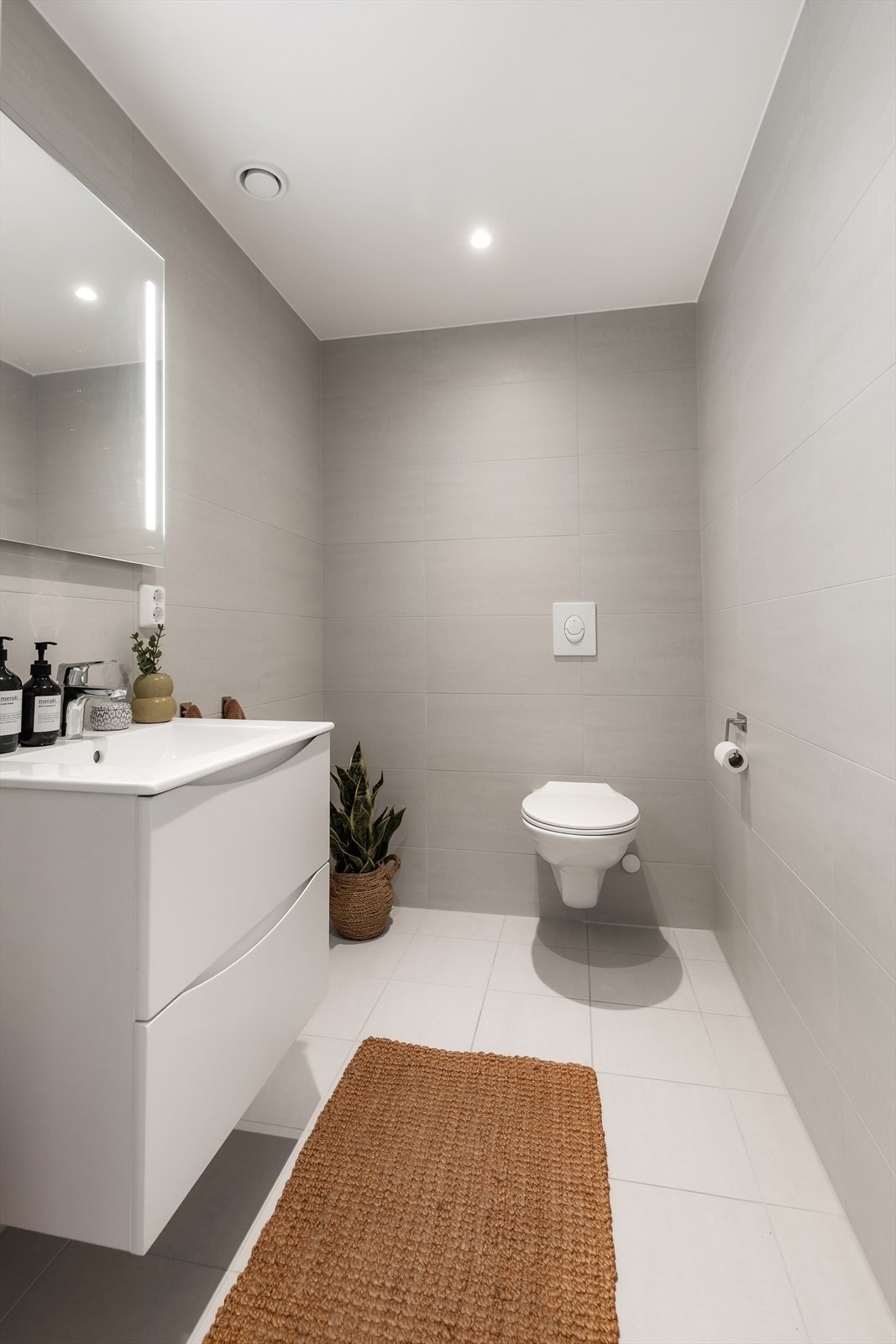 Toalettrom fra byggeår. Flislagt gulv med gulvvarme og flislagte vegger. Malt himlingsflate med downlights. Servant med ett-greps armatur og speil. Innebygd sisterne med vegghengt toalett. Avtrekksventil i himling. Galleribilde