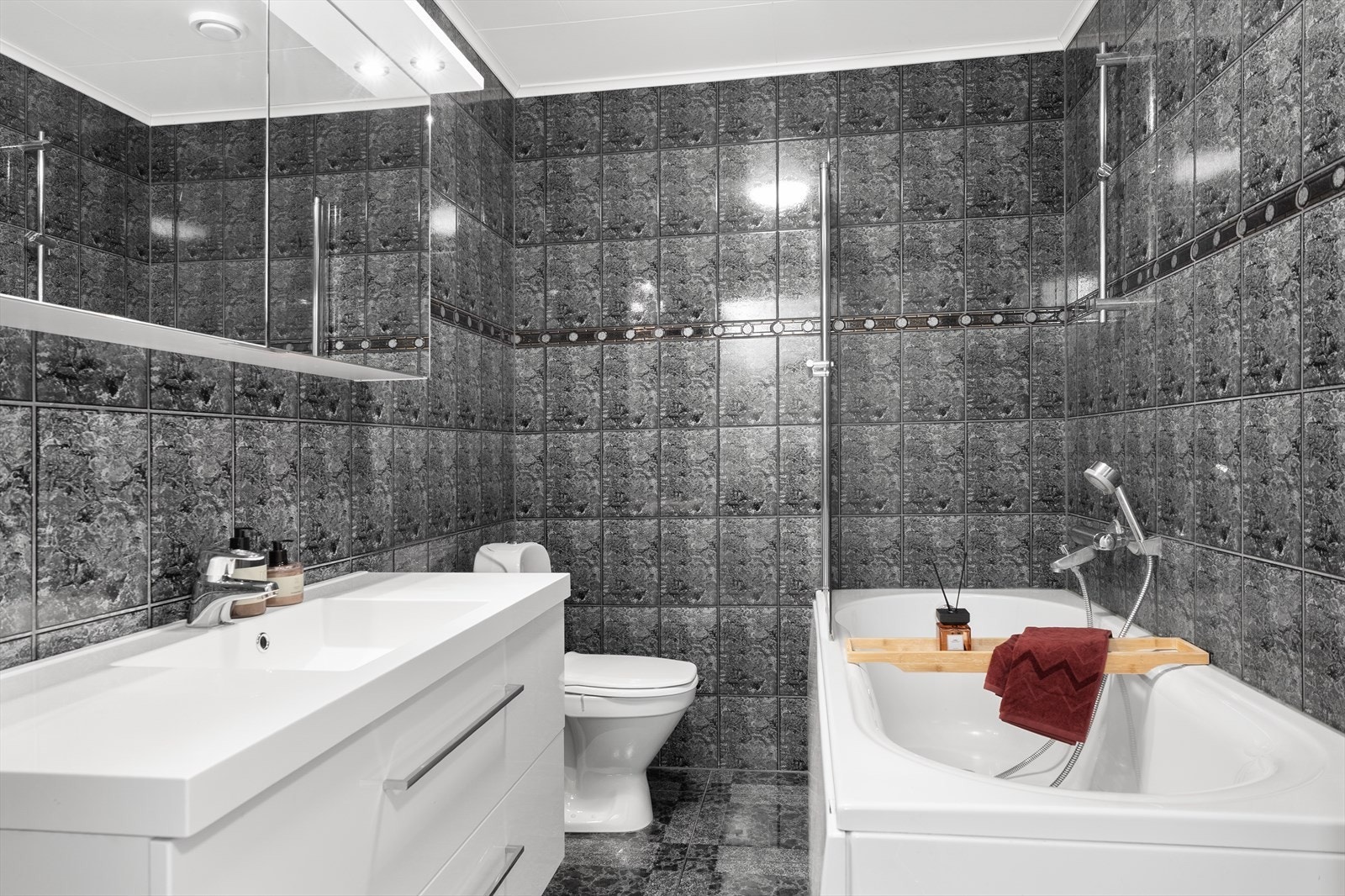 Romslig, helfliset bad som er innredet med hvit baderomsinnredning, gulvmontert toalett og badekar med dusjvegg (ny i 2020) Galleribilde