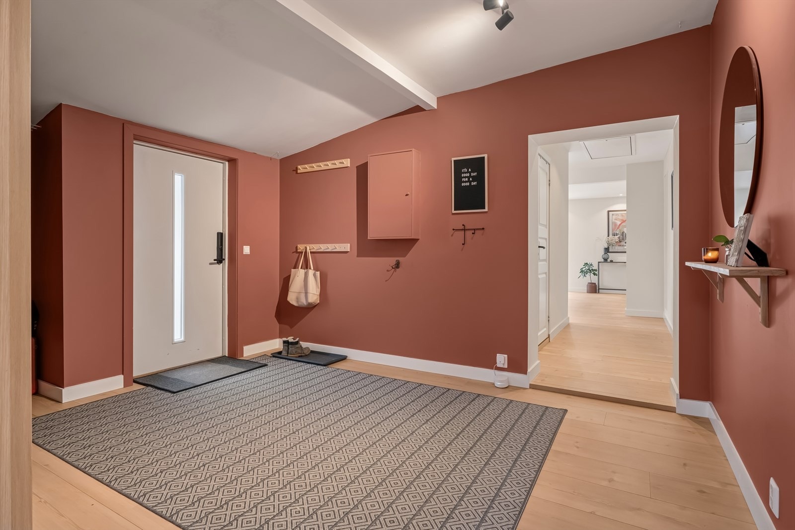 Boligen har en stilren hvit ytterdør med glassfelt som slipper inn et behagelig og naturlig lys, og skaper en innbydende atmosfære i entréen Galleribilde