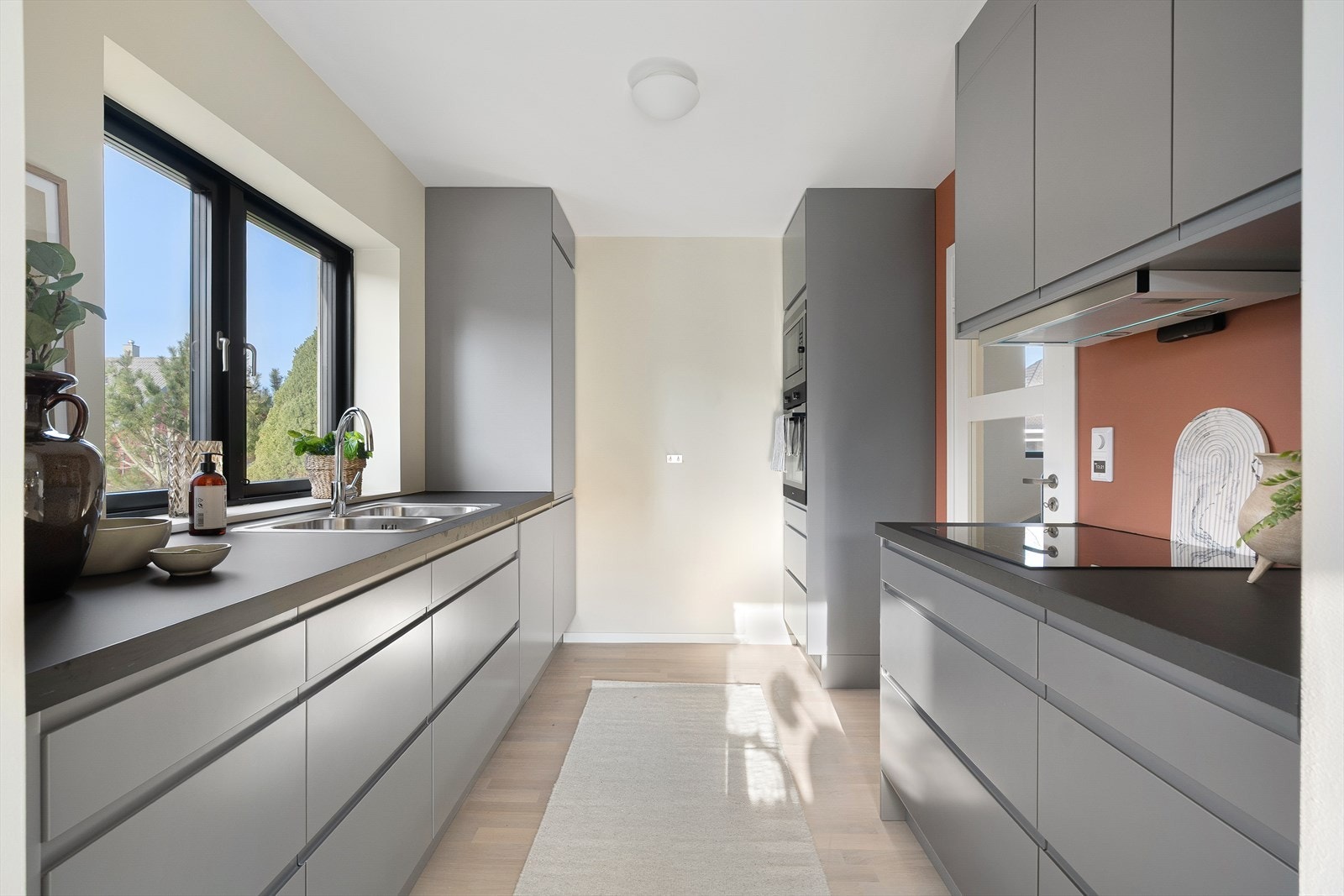 Kjøkkenet har moderne uttrykk med slette grå fronter og benkeplate i mørk kompositt for en stilren arbeidsflate. Galleribilde