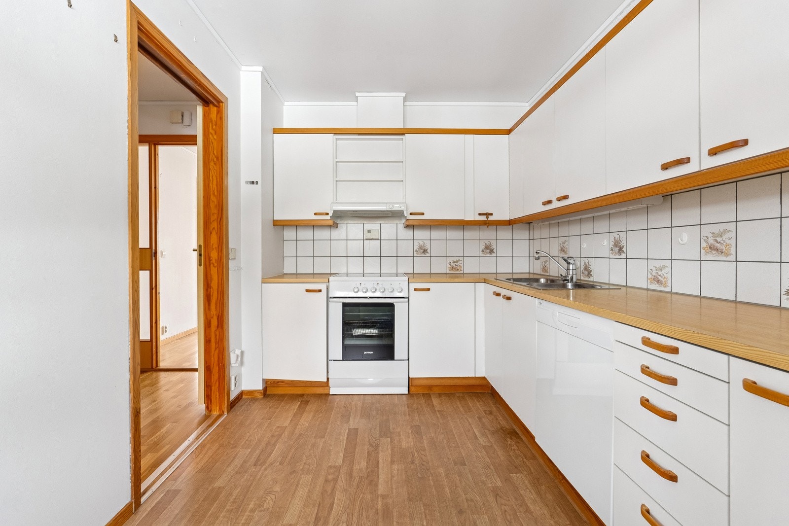 Kjøkkeninnredning med slette folierte fronter, laminat benkeplate m/fliser over, dobbel oppvaskkum, ventilator og opplegg for oppvaskmaskin. Galleribilde