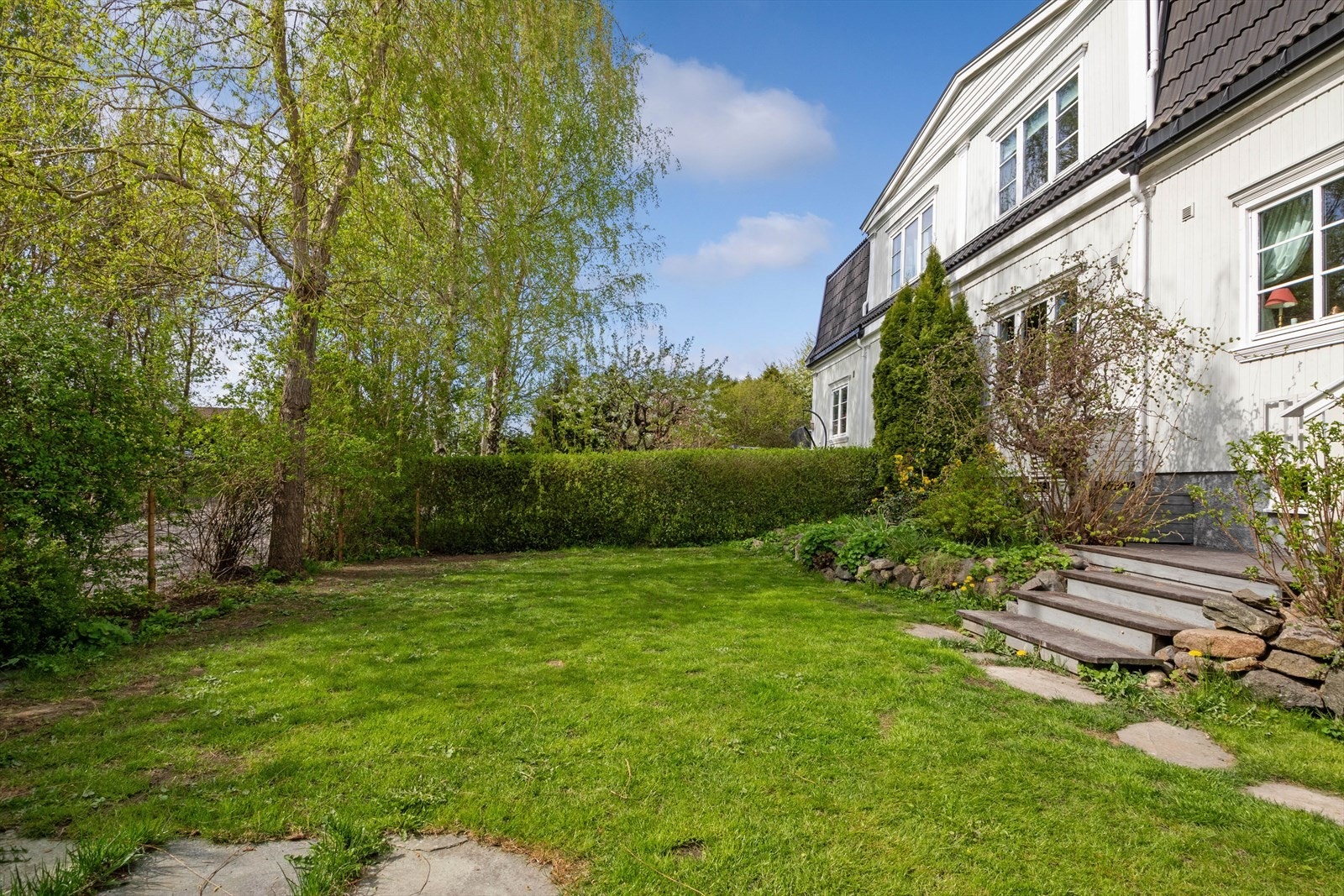 Tomten er svakt skrånende og er preget av en hyggelig hage med plen, hekker og diverse beplantning som skjermer for innsyn. Galleribilde