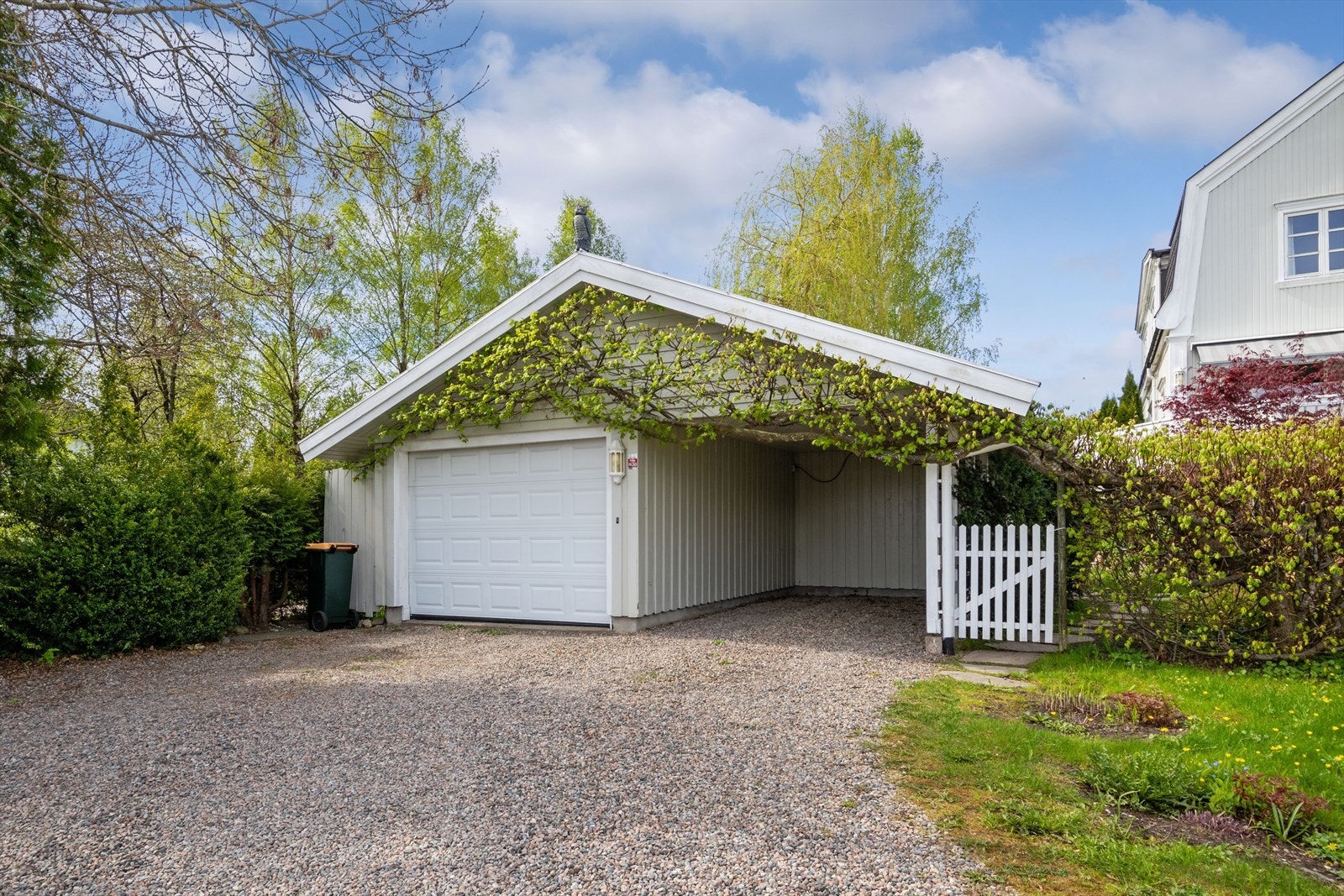 Gårdsplassen er gruslagt og leder frem til en romslig garasje med tilhørende carport. Galleribilde