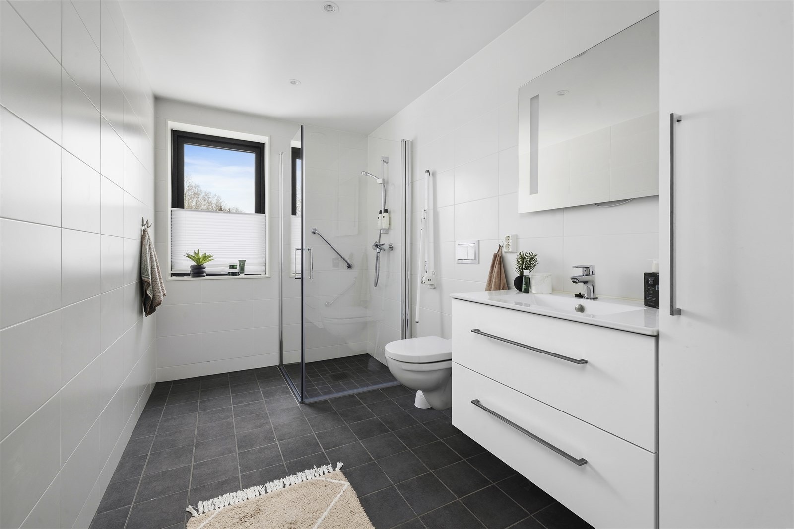 Baderommet har nøytrale fliser på vegger og gulv, med varmekabler Galleribilde