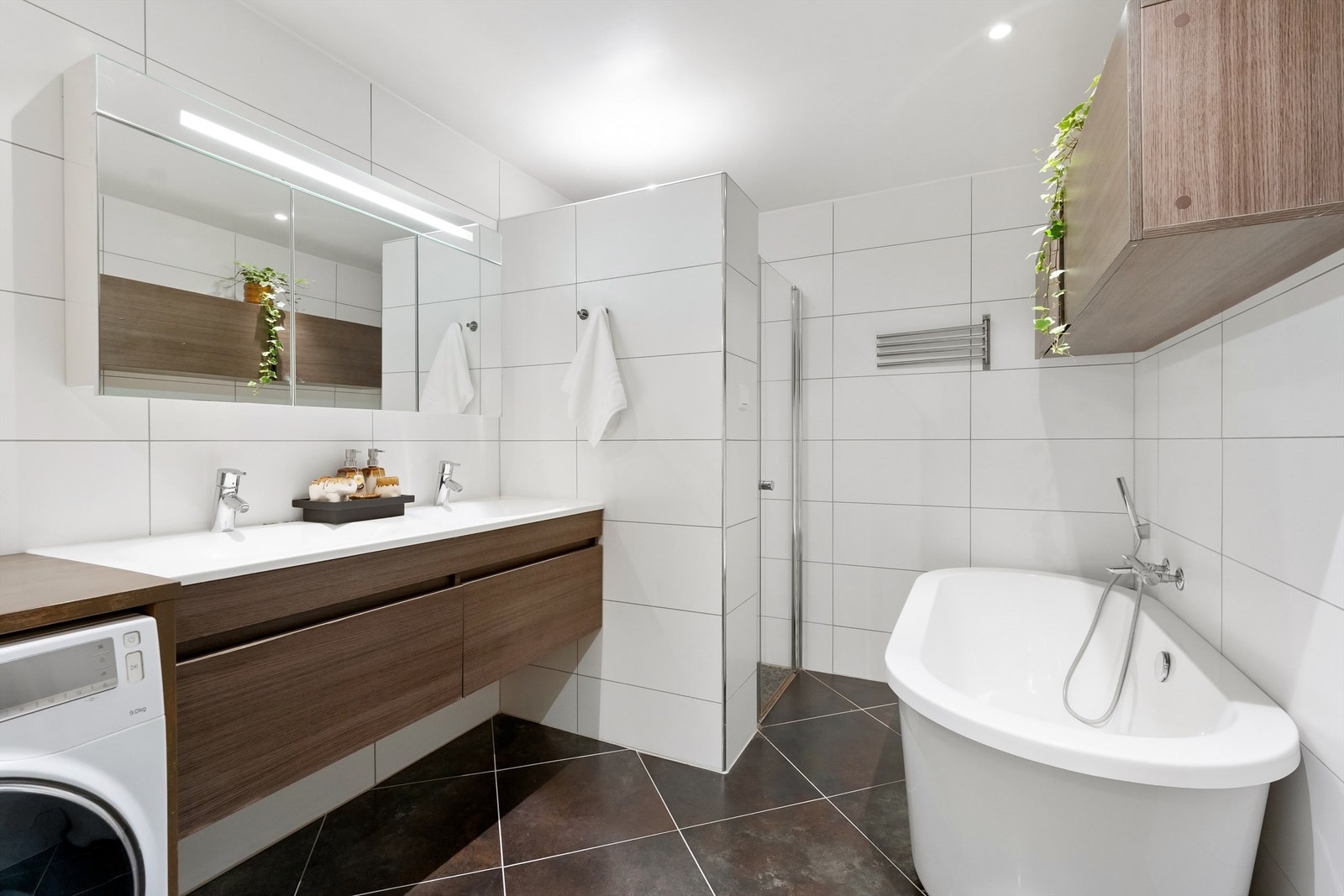 Badet har vegghengt toalett, vegghengt servantskap med dobbel nedsenket servant, vegghengt speilskap med overbelysning og dusjsone med innfellbare glassdører, hånddusj og regndusj, samt badekar Galleribilde