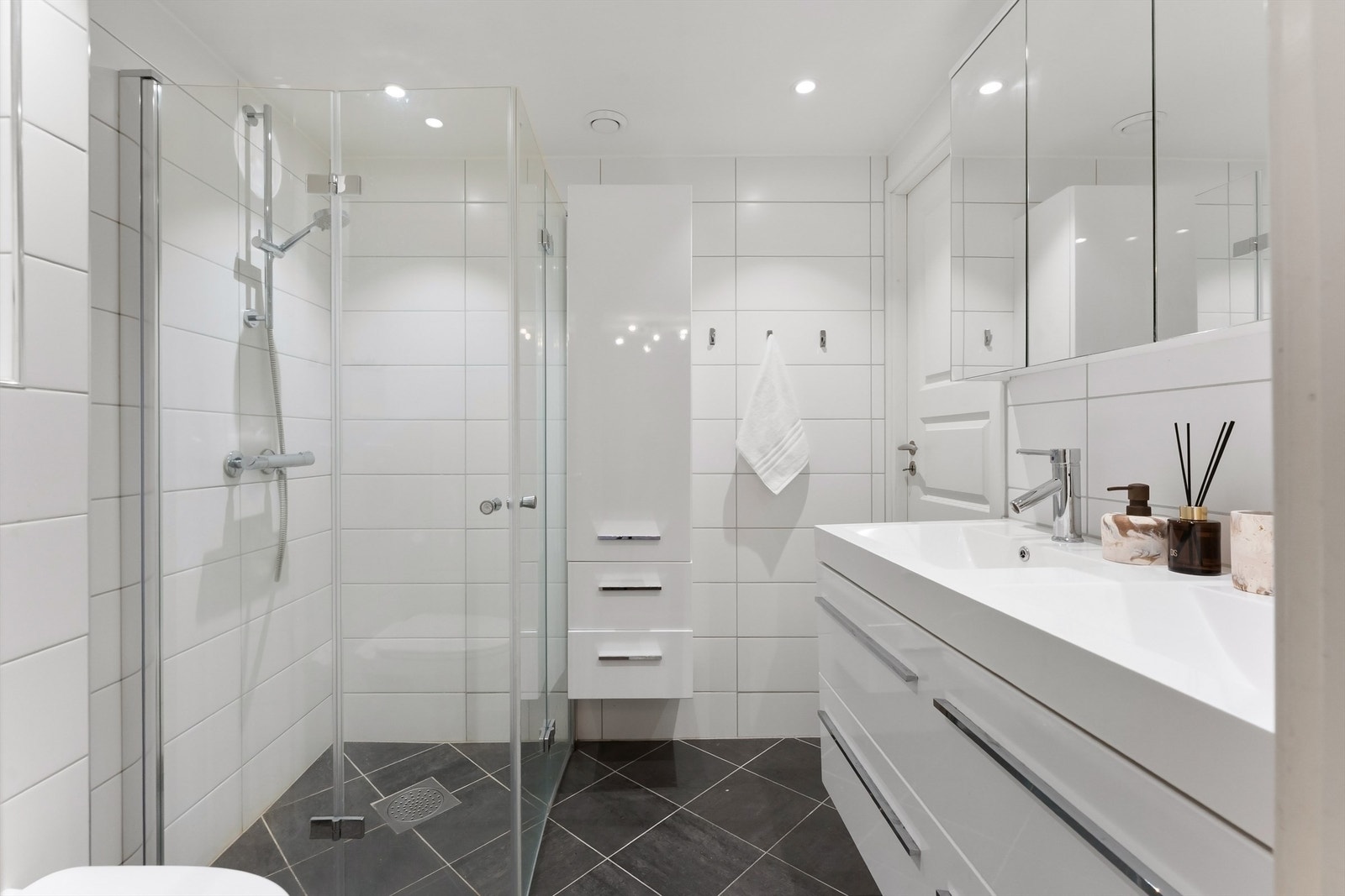 Badet har vegghengt toalett, vegghengt servantskap med dobbel nedsenket servant, vegghengt speilskap med overbelysning og dusjsone med innfellbare glassdører Galleribilde