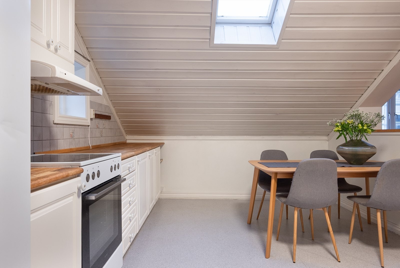 Kjøkkeninnredningen fyller to vegger _ med benkeplater i heltre, hvite fronter og frittstående hvitevarer. Her er et mindre veggvindu, men hoveddelen av dagslyset strømmer inn fra takvinduet. Galleribilde