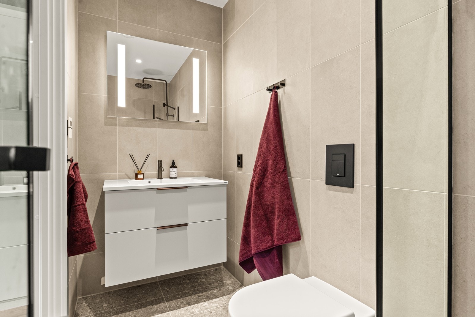 Badet er utstyrt med tidsriktig servantinnredning med lagringsplass i skuffene, og det er speil med LED-lys over servanten. Videre er det vegghengt toalett og dusjhjørne med glassvegger. Galleribilde