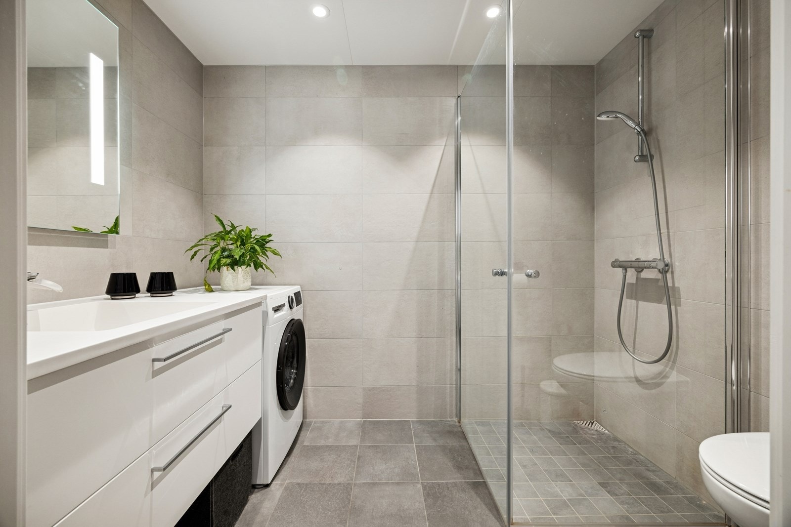 Pent, flislagt bad med dusjhjørne med glassdører og opplegg for vaskemaskin. Galleribilde