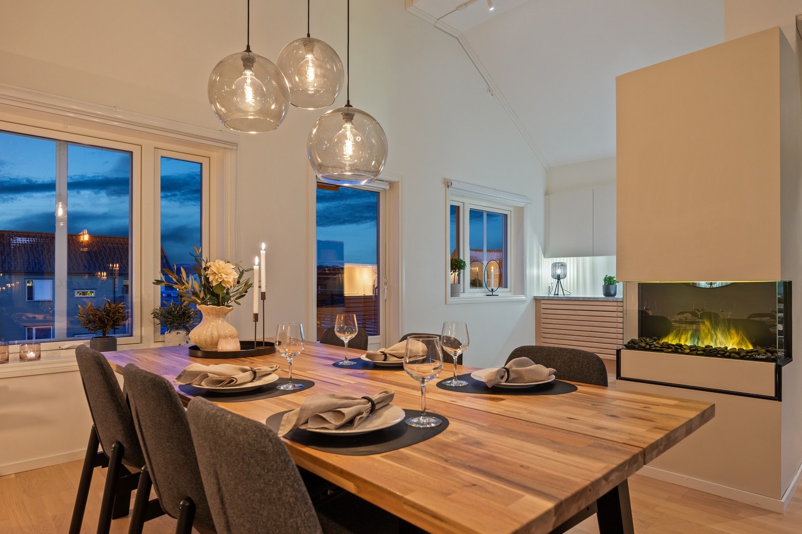 Når kvelden senker seg, fremstår kjøkken og spiseplass som et varmt og innbydende samlingspunkt. Den dempede belysningen, kombinert med store vindusflater og utsyn mot omgivelsene, gir rommet en rolig og elegant atmosfære. Galleribilde