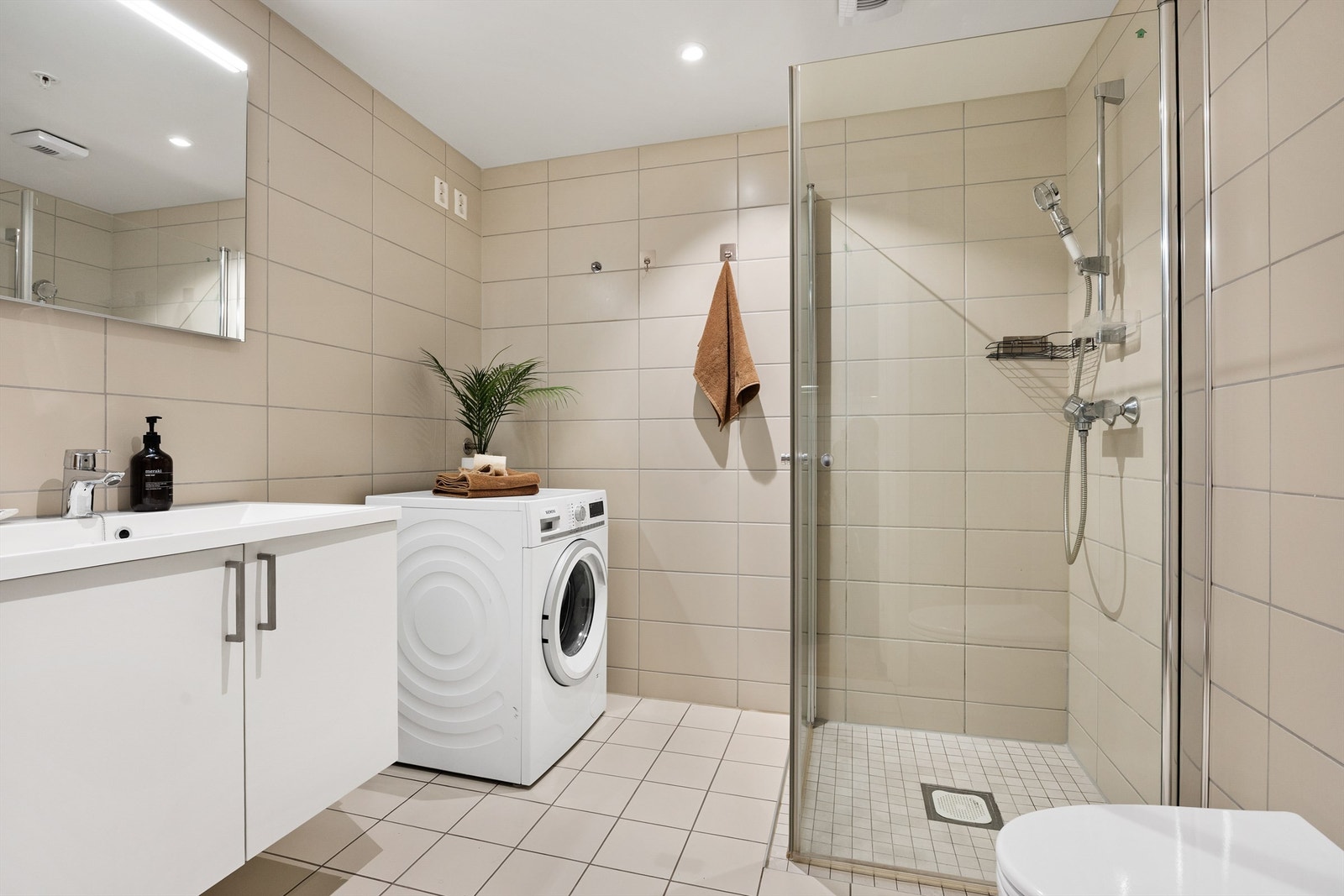 Rommet er innredet med vegghengt servantinnredning med dører, dusjhjørne med glassdører og vegghengt toalett. Galleribilde