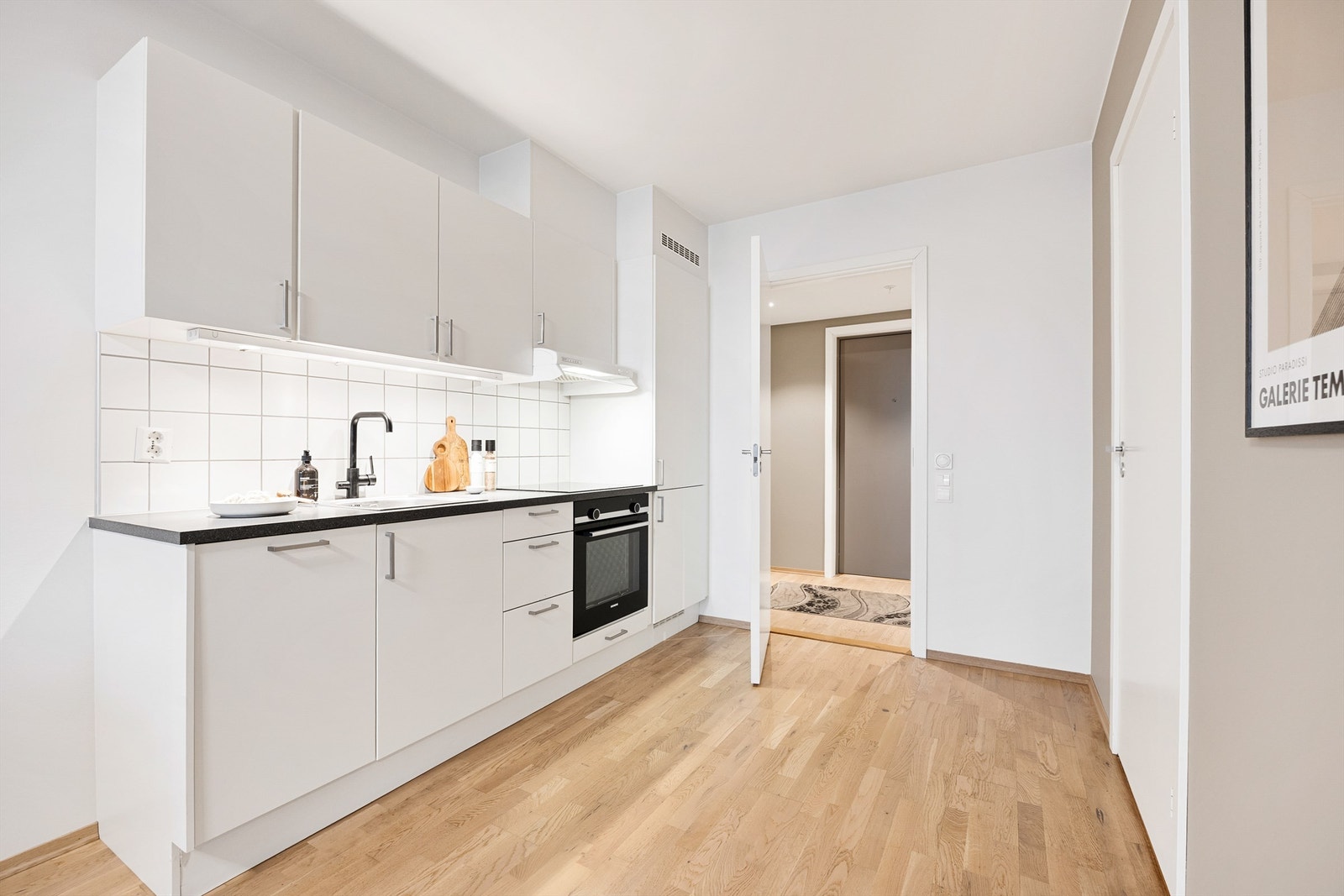 Kjøkkeninnredningen er fra byggeår med glatte fronter, laminat benkeplate og fliser mellom kjøkkenbenk og overskap. Galleribilde