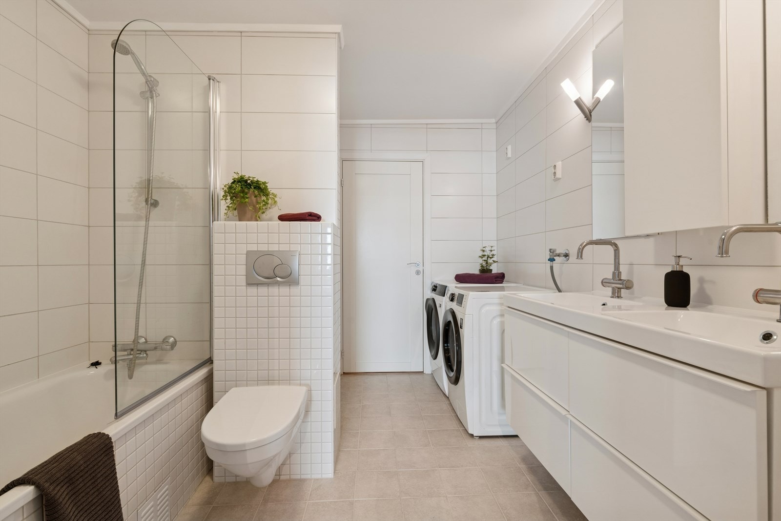 Baderommet har fliser på vegger og gulv med varmekabler i gulvet. Rommet er innredet med to nedfelte servanter, veggmontert toalett, badekar og dusjhjørne. Det er også opplegg for vaskemaskin Galleribilde