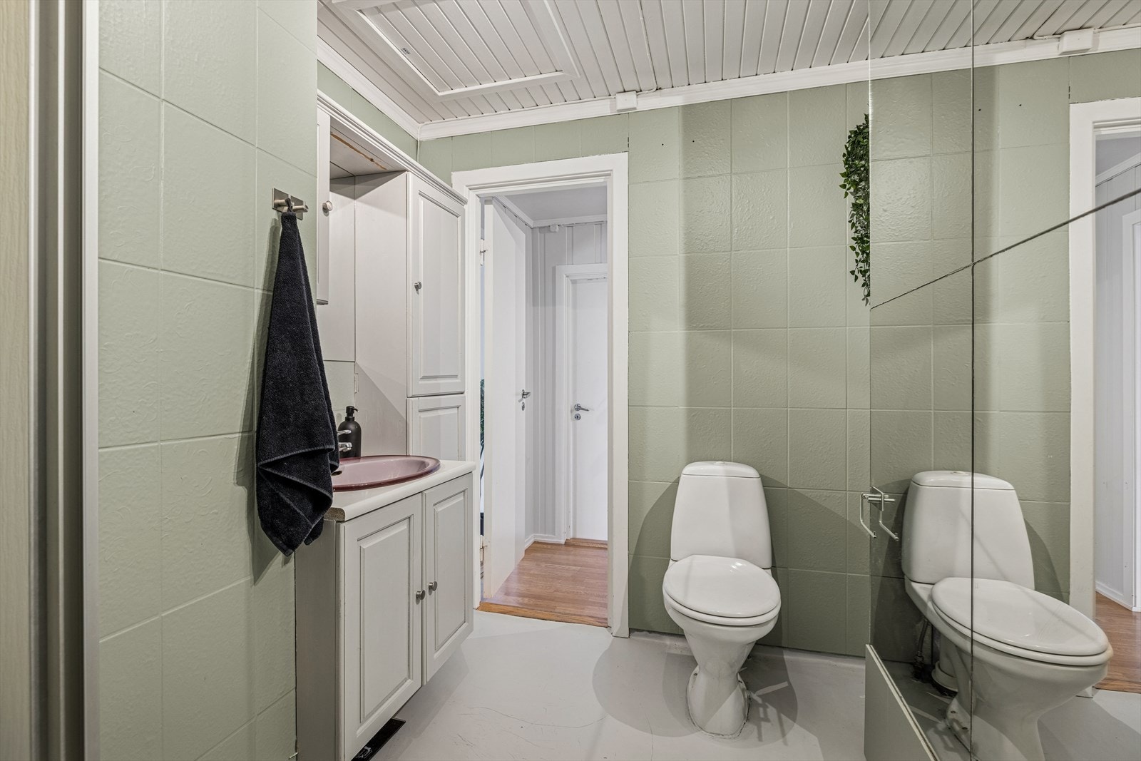 Veggene på baderommet har malte fliser og himlingen er kledd med malt panel. Gulvet består av malt belegg lagt på betong med oppkant. Galleribilde