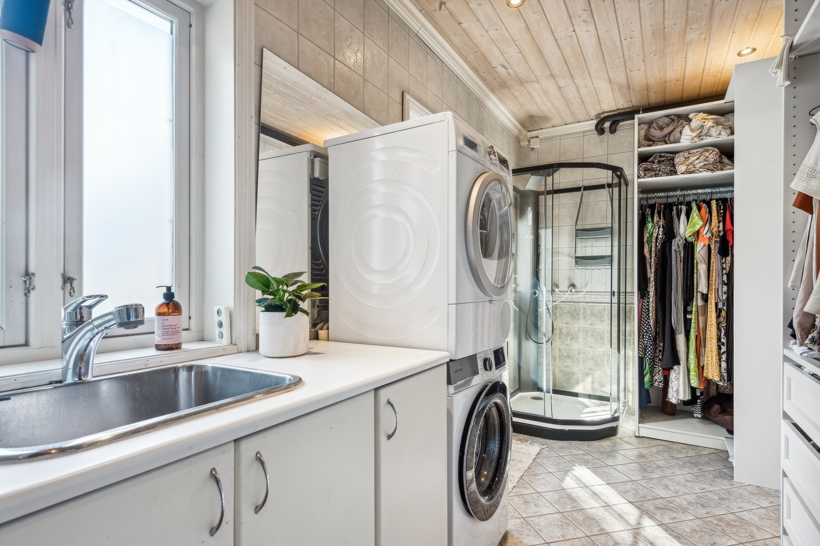 Praktisk baderom/vaskerom med dusjkabinett, nedfelt servant og åpne garderobeskap. Det er opplegg for vaskemaskin og plass til tørketrommel. Galleribilde