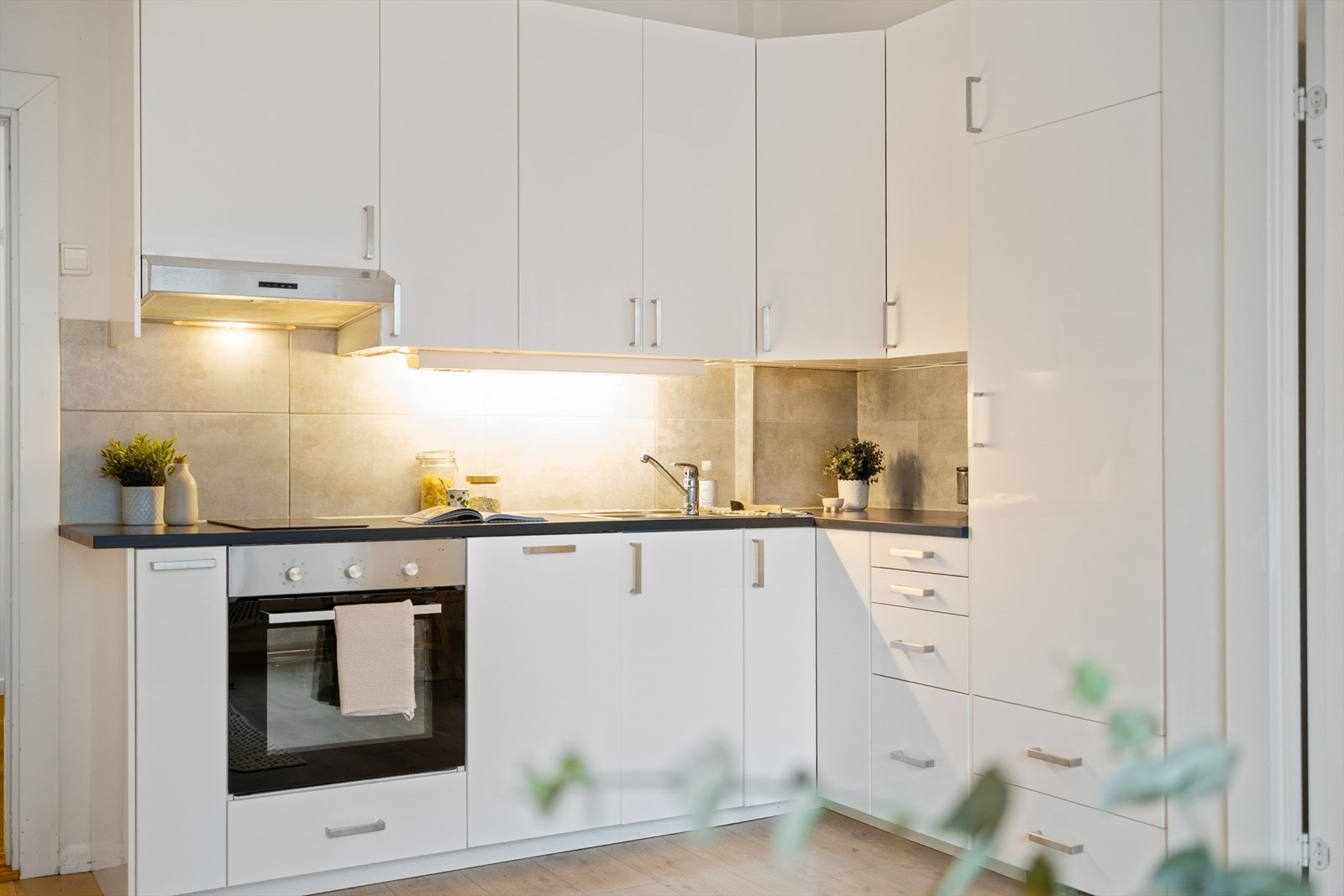 Tidsriktig glatt innredning fra IKEA, soft close, fliser over benk, armatur, laminat benkeplate med nedfelt stålkum og keramisk topp, integrert komfyr, oppvaskmaskin (smal type), kjøleskap. Det er kjøkkenventilator med kullfilter. Galleribilde