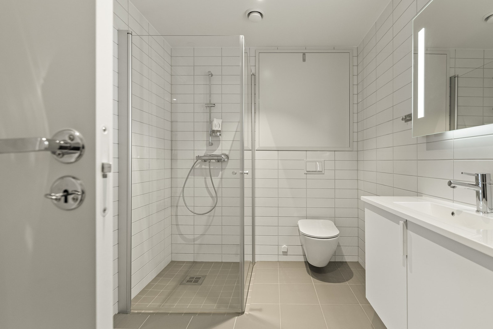 Badet er innredet med dusjhjørne, servantskap, speil med lys, vegghengt klosett og har opplegg til vaskemaskin Galleribilde