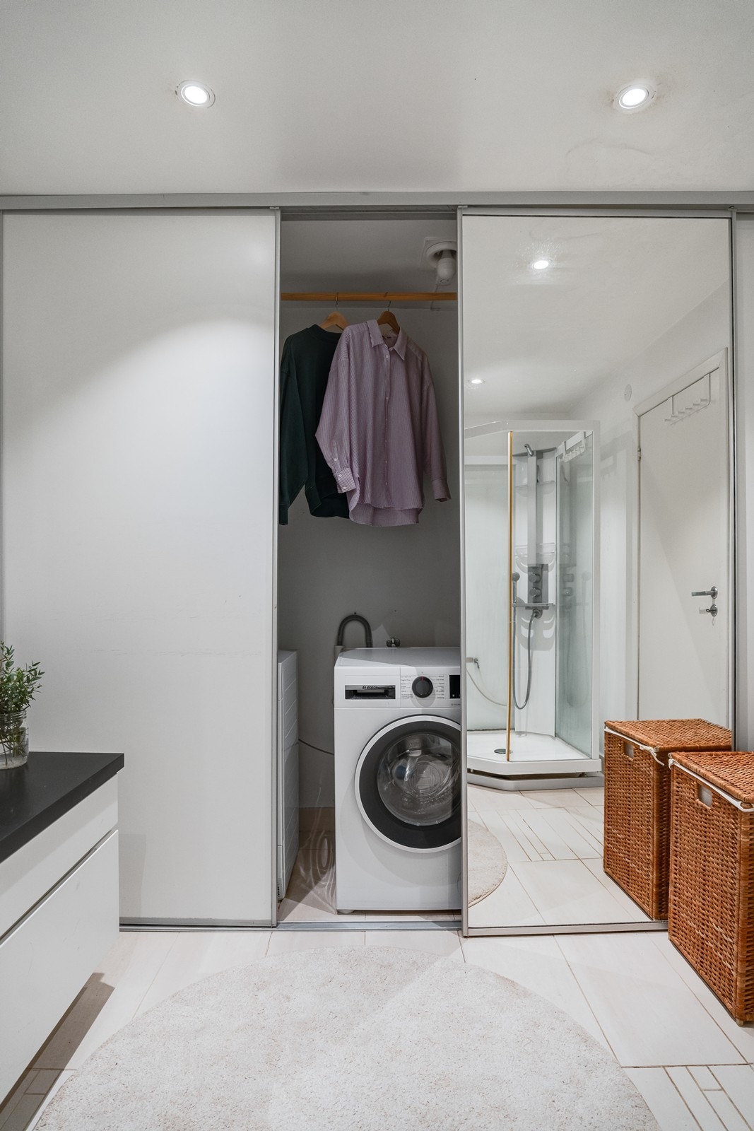 Praktisk vaskesone integrert i badet, lukket med store skyvedører, med opplegg for vaskemaskin og tørketrommel samt smarte oppbevaringsløsninger. Galleribilde