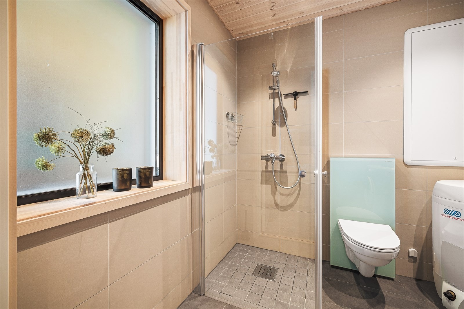 Rommet er utstyrt med dusjhjørne med glassdører, servant med skuffeinnredning, veggmontert toalett med utenpåliggende sisterne og opplegg for vaskemaskin. Galleribilde