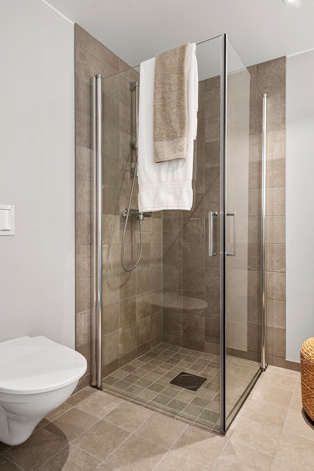 Romslig dusjsone med moderne glassvegger og flislagte overflater i tidløse fargetoner. Praktisk løsning med god plass og et rent, elegant uttrykk. Galleribilde