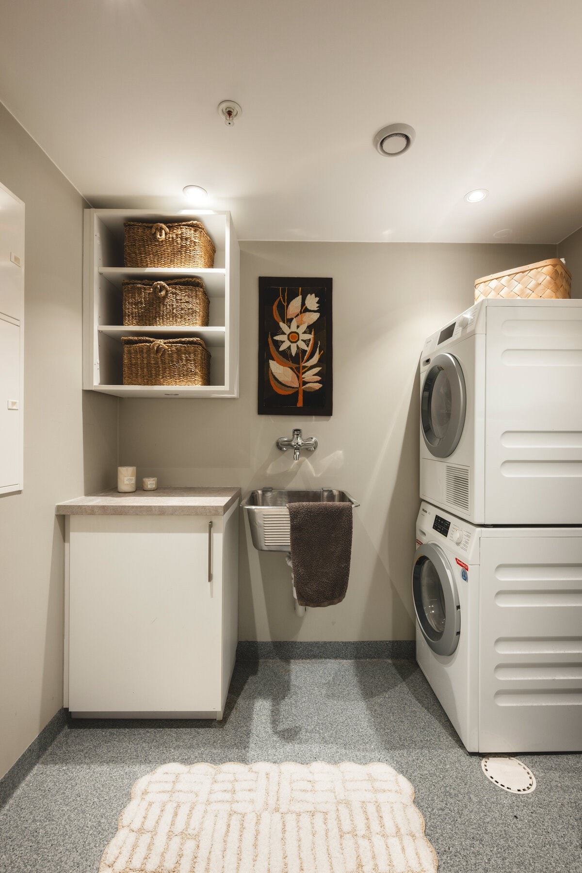 Praktisk vaskerom med vaskemaskin, tørketrommel, vaskekum og skapplass. Vegghyller gir ekstra oppbevaringsmuligheter. Galleribilde