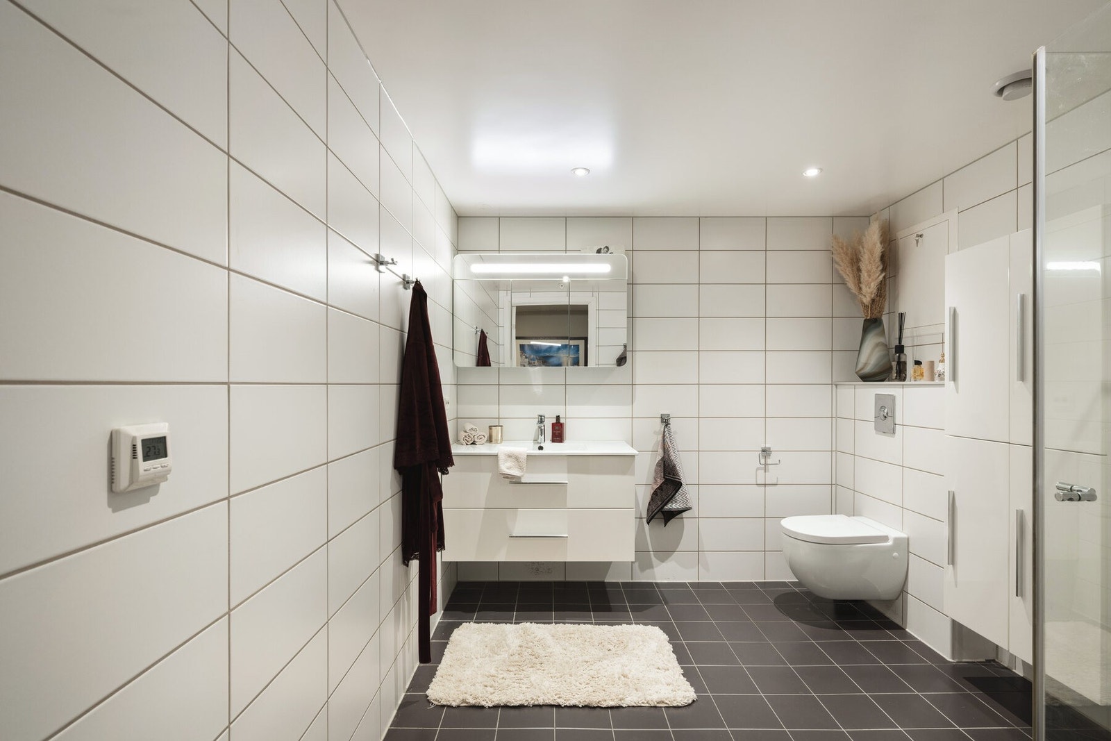 Badet har hvite fliser, vegghengt toalett og dusj med glassdør. Enkelt og moderne med god belysning. Galleribilde