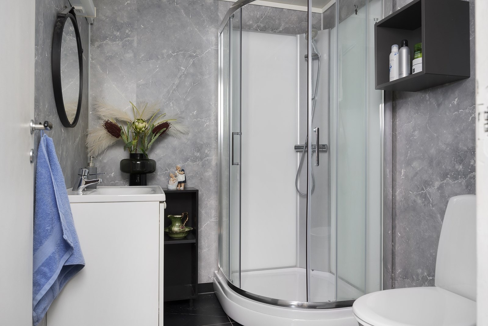 Baderom som er innredet med servant nedfelt i benkeskap, vegghyller, speil, toalett og dusjkabinett Galleribilde