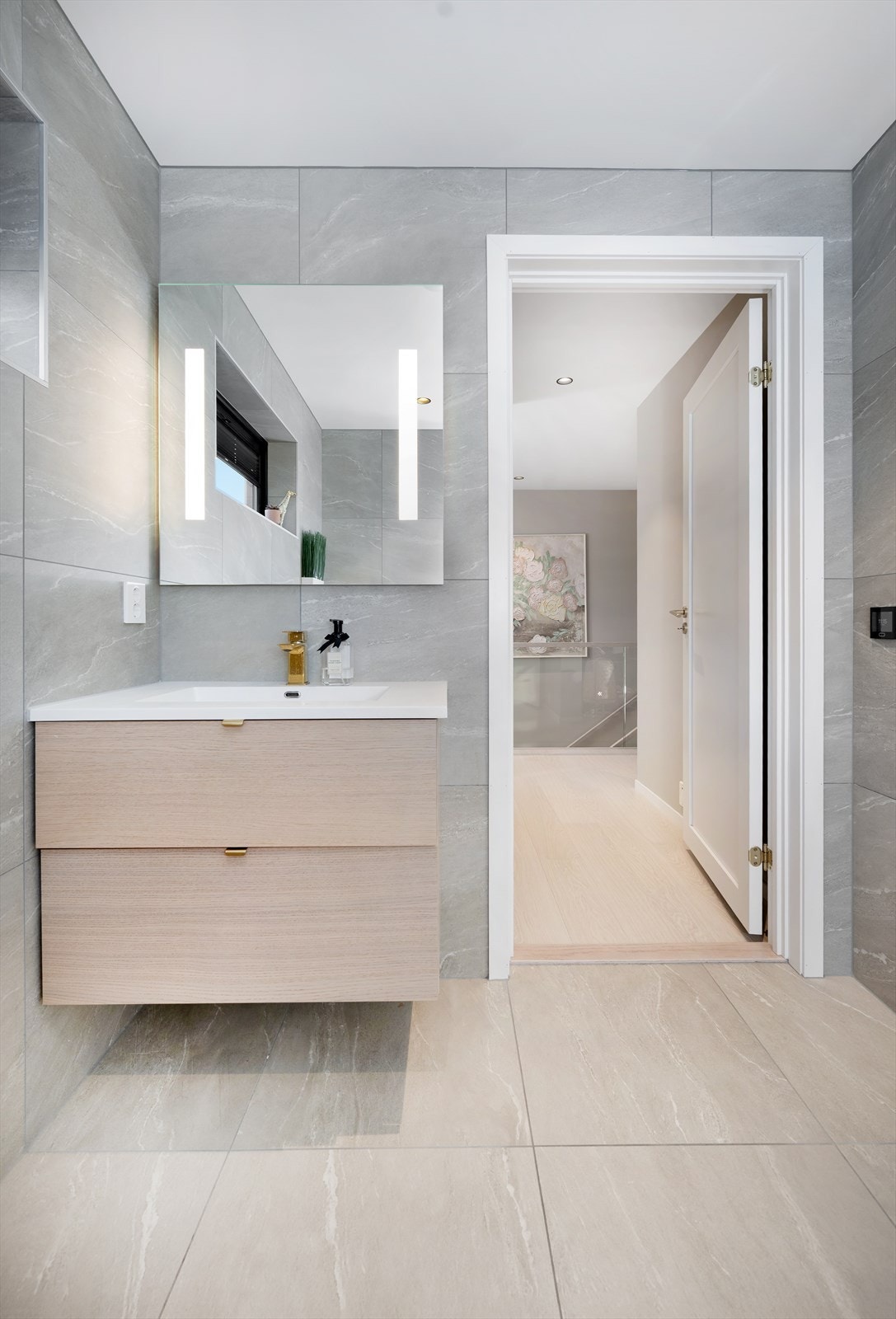 Badet har baderomsinnredning med heldekkende vask, speil med lys, vegghengt toalett og dusj med glassdører Galleribilde