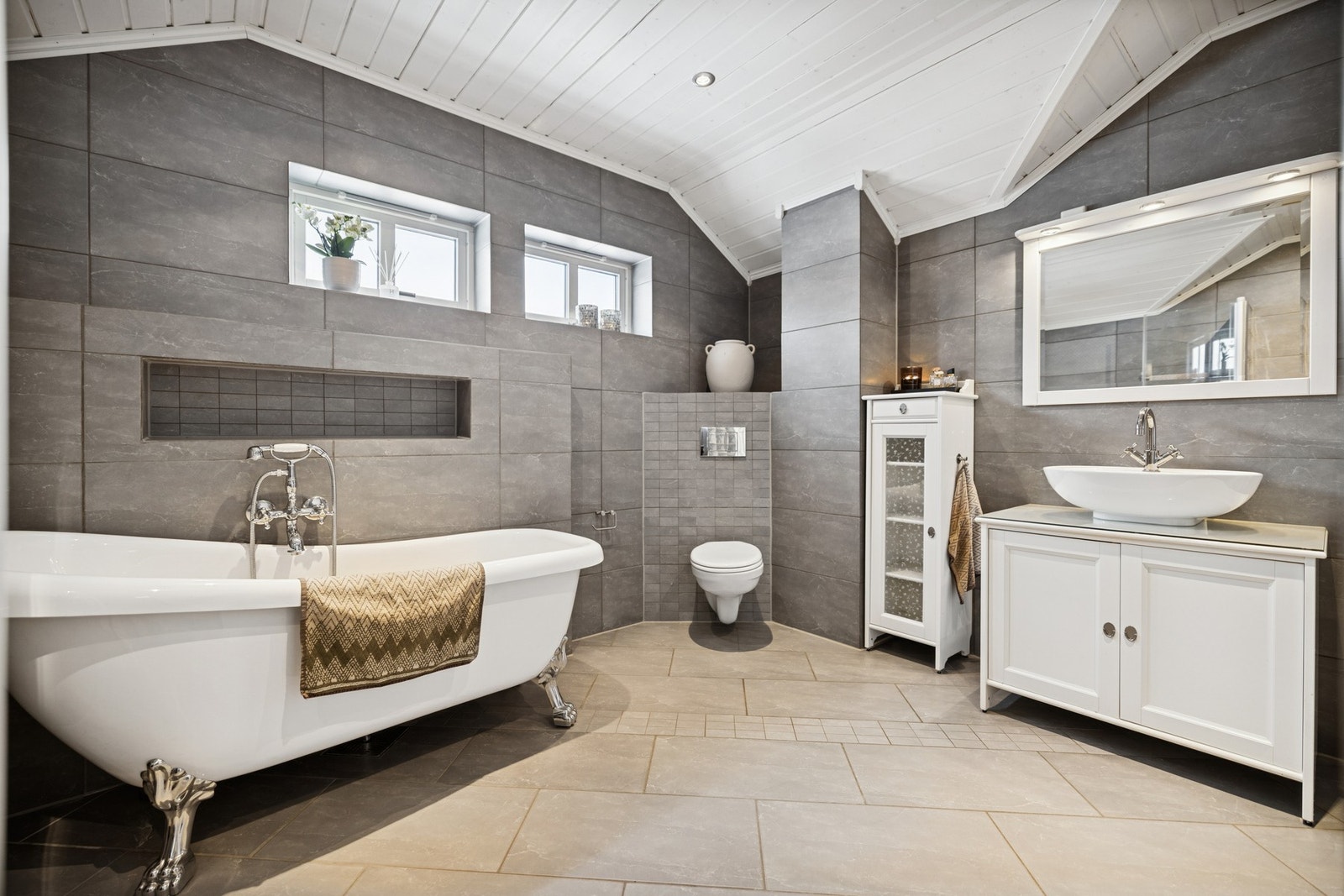 Rommet har både badekar og dusjhjørne med glassbyggerstein og glassdør, noe som gir en stilren og praktisk løsning. Downlights i tak sørger for god belysning, og elektriske varmekabler i gulvet gir ekstra komfort. Galleribilde