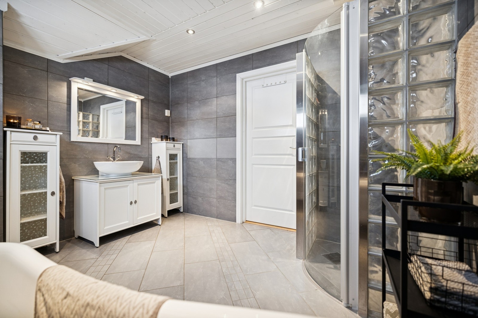 Klassisk bad i 2. etasje med flislagte gulv- og veggflater, og himling med malt panel. Badet er innredet med lys baderomsinnredning, toppmontert servant og speil på vegg, samt vegghengt WC. Galleribilde