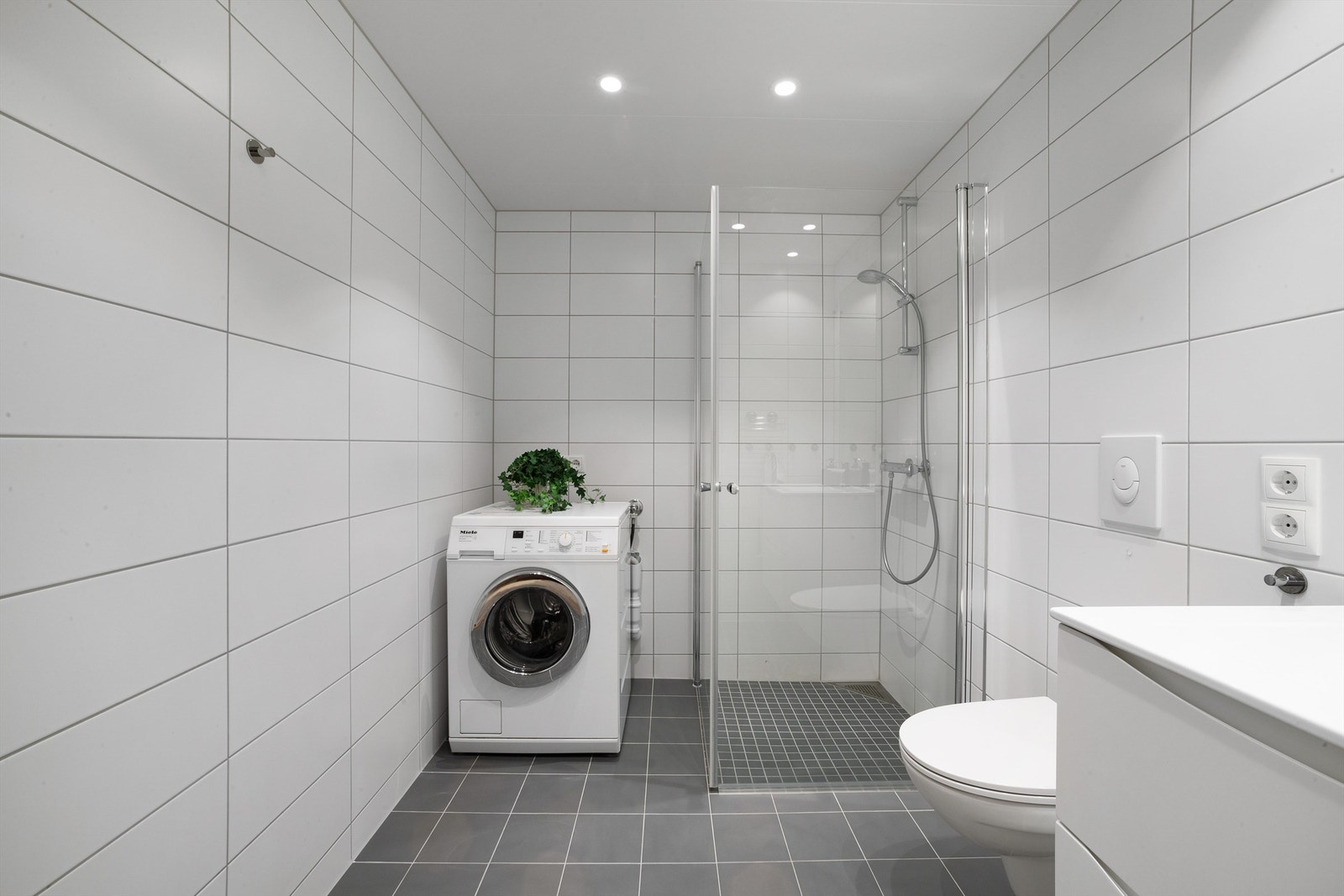 Flislagt, romslig bad med dusjhjørne og opplegg for vaskemaskin Galleribilde
