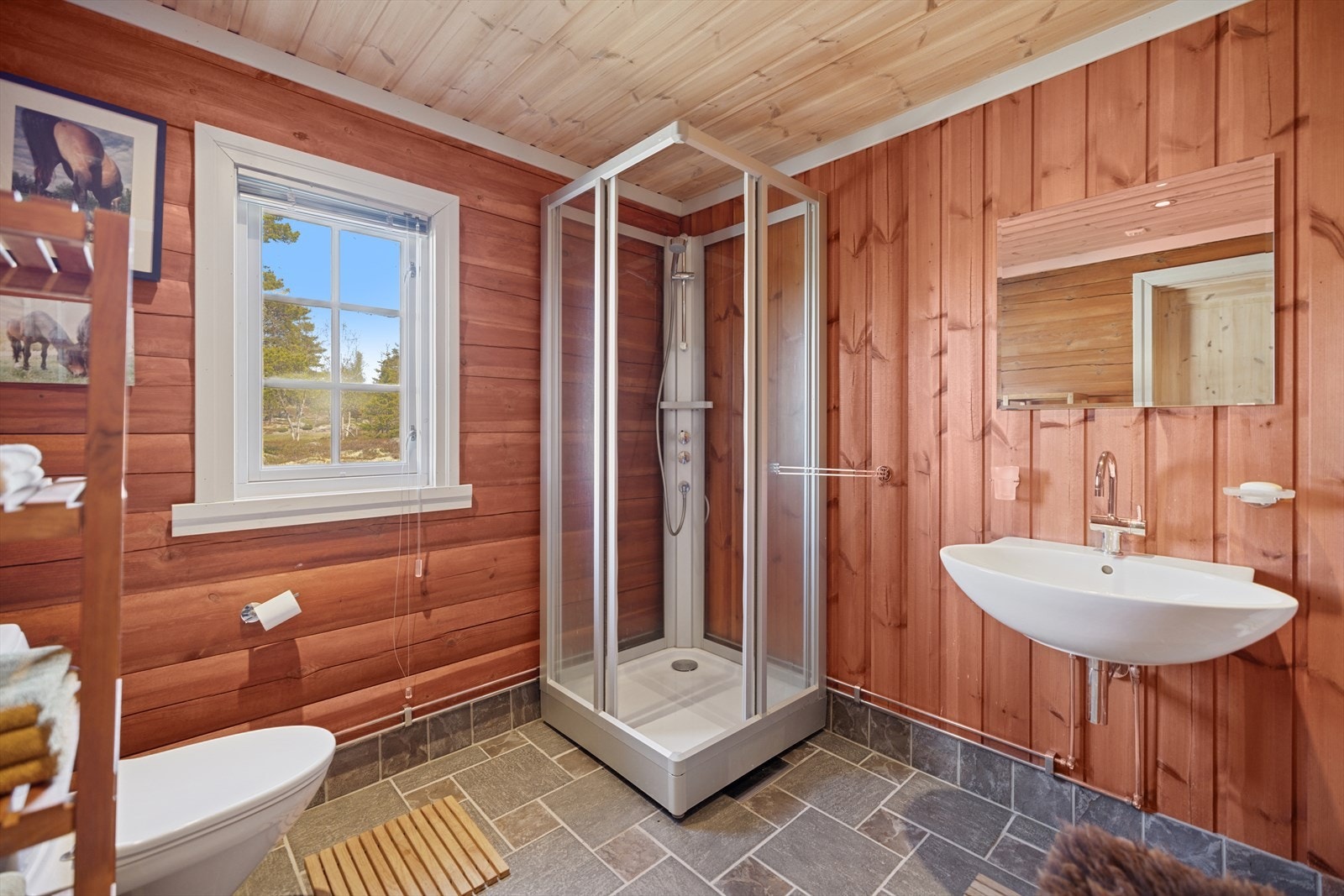 Badet har et delikat, flislagt gulv med varmekabler. Dusjhjørne, toalett og servant Galleribilde