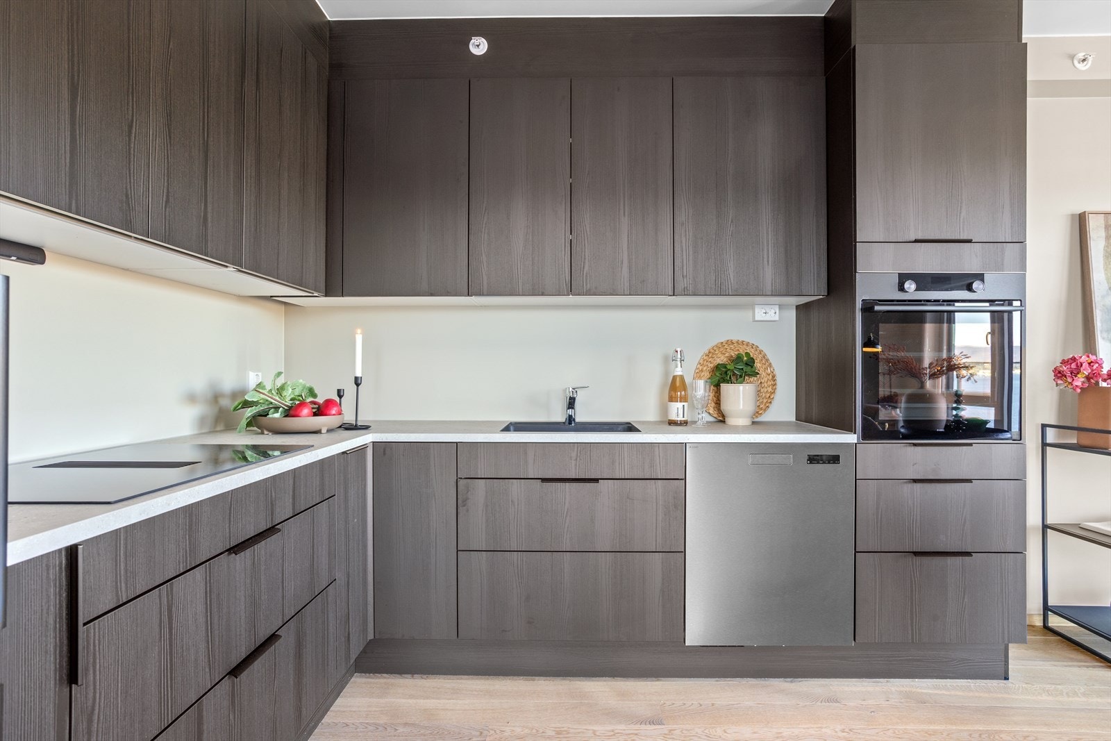 Kjøkkenet ligger i en L-form og har integrert stekeovn, koketopp og oppvaskmaski. Laminert benkeplate med underlimt kum. Galleribilde