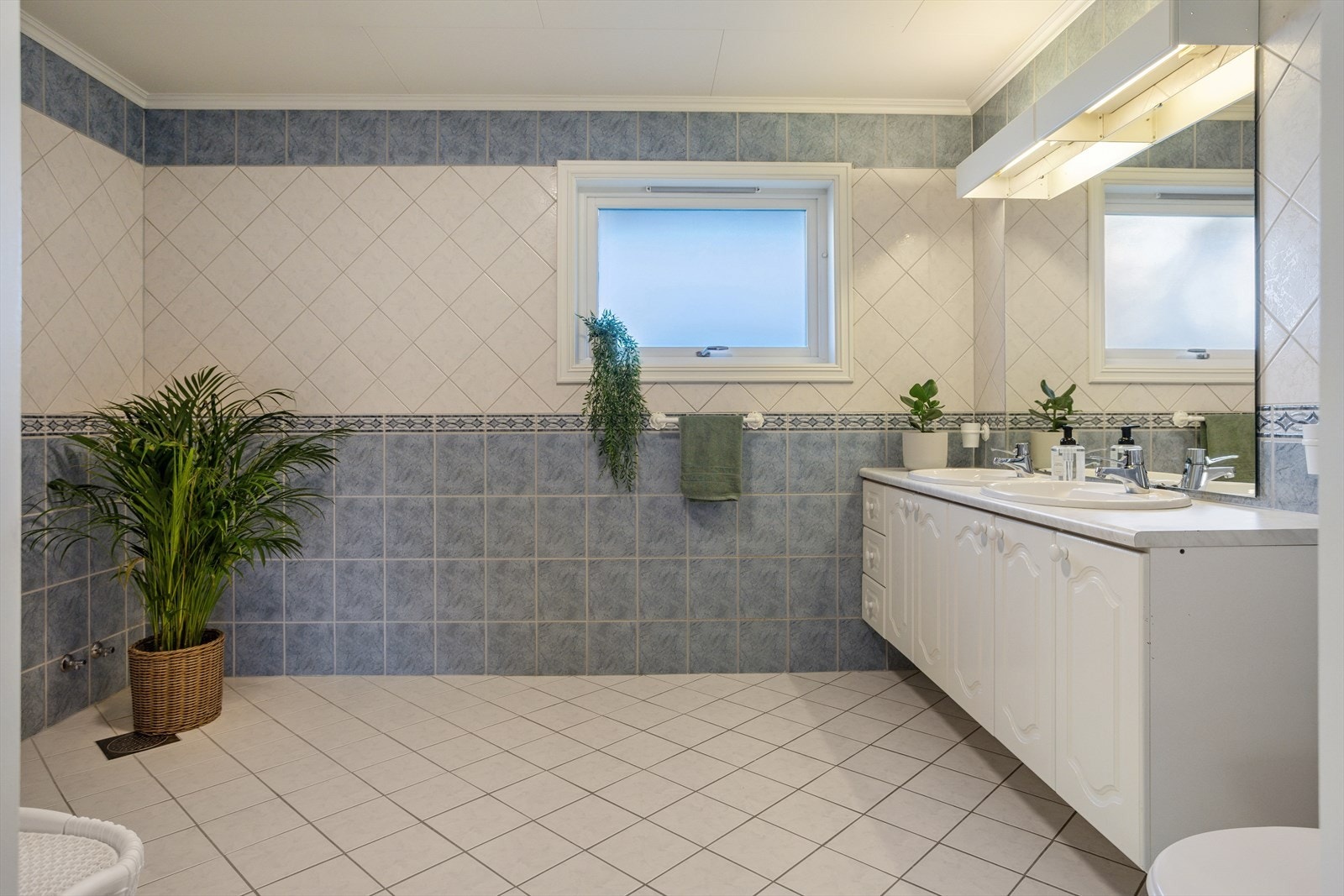 Stort, helfliset bad på ca. 9 m² med elektriske varmekabler og møblement med to servanter. Galleribilde