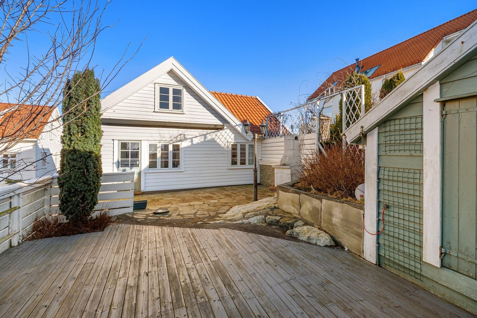 Bildet viser fasade fra baksiden. Tomten er lettstelt med områder som er både skifterbelagte og flater av tre. Galleribilde