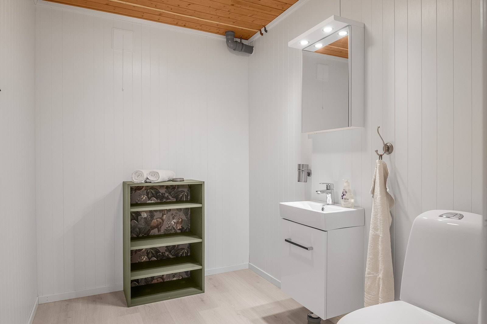 Lyst toalettrom i kjeller som er utstyrt med servantskap, speilskap med belysning over og gulvstående toalett (nytt i 2025). Galleribilde