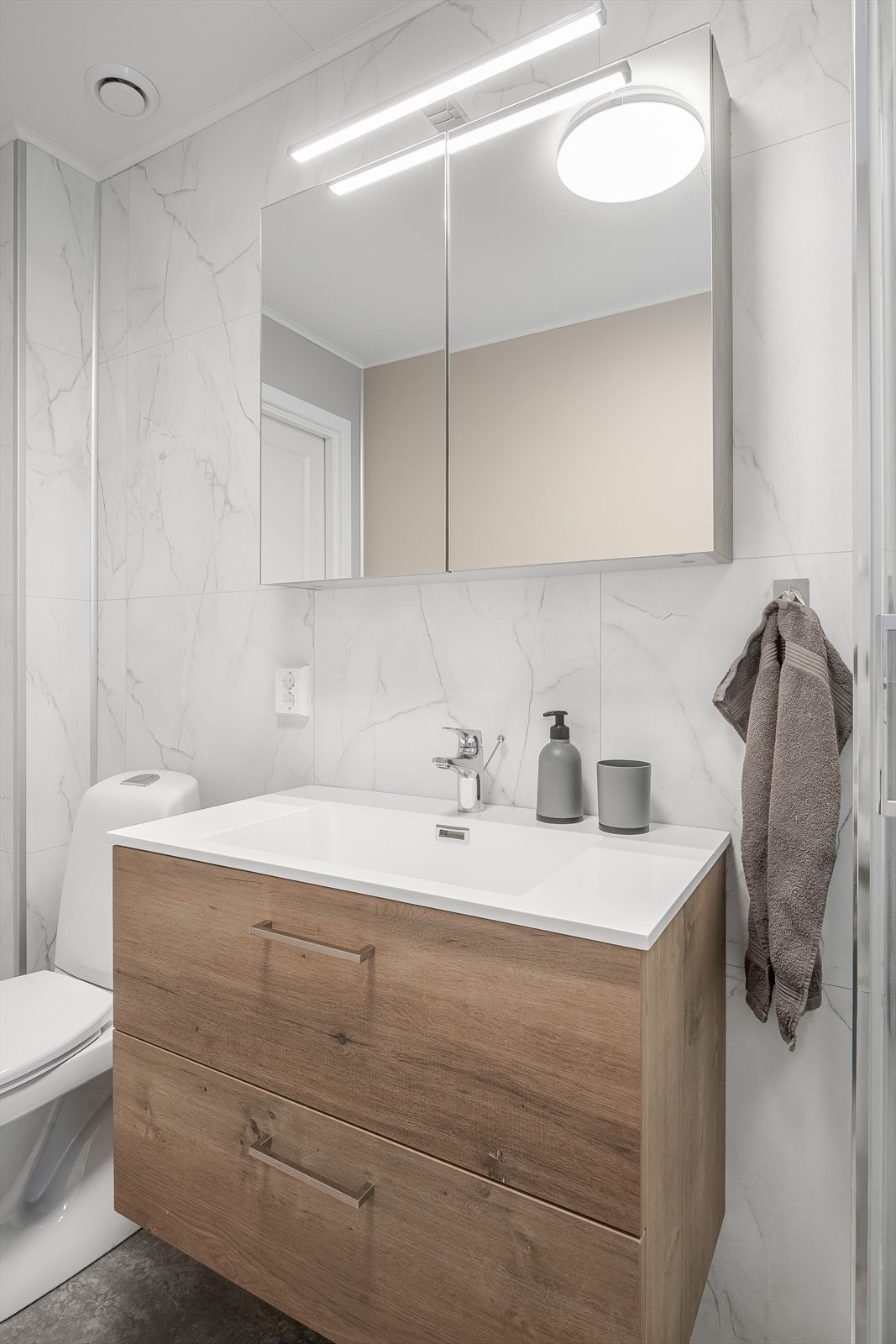 Pen baderomsinnredning med skuffer og heldekkende servant, speilskap med belysning over. Baderommet er også utstyrt med dusjkabinett og gulvstående toaett. Galleribilde