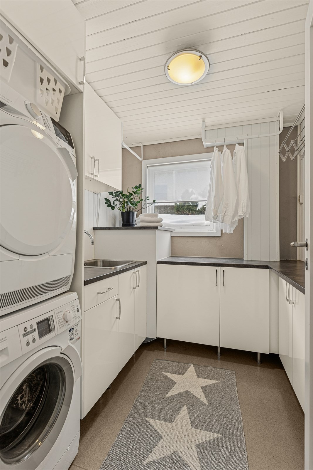 Vaskerommet er utstyrt med opplegg for vaskemaskin og innredning som inkluderer skap, benkeplate og utslagsvask. Galleribilde