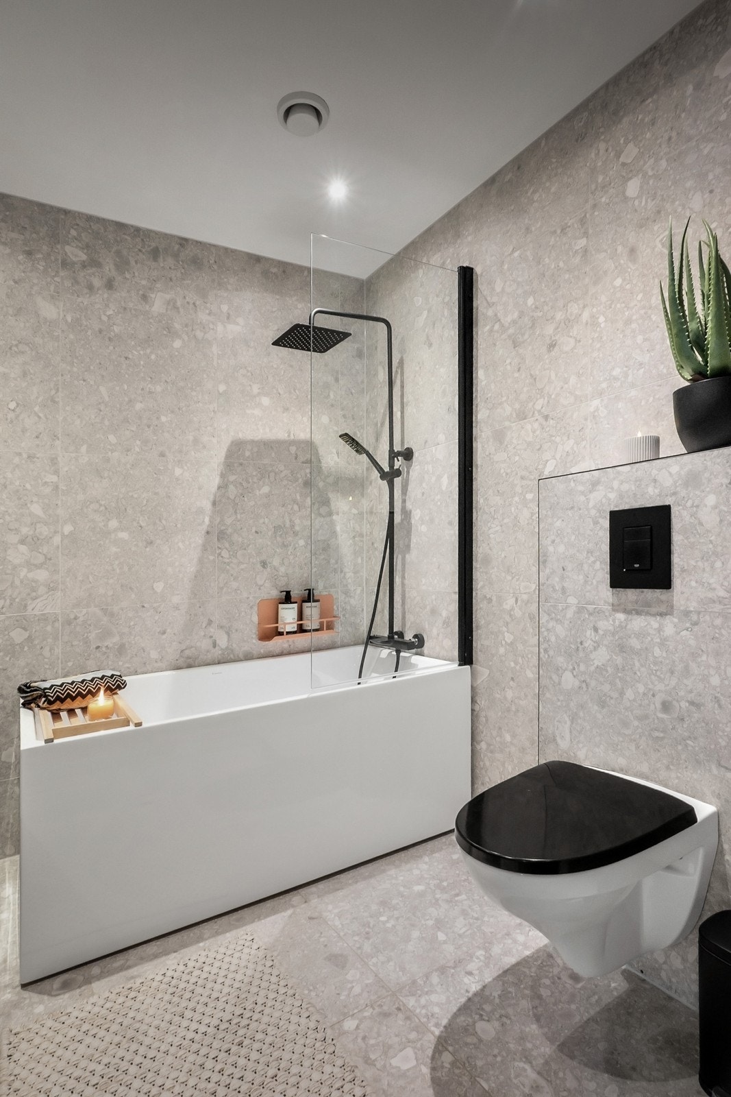 Badet er videre utstyrt med vegghengt toalett samt badekar med takdusj og hånddusj i sort armatur Galleribilde