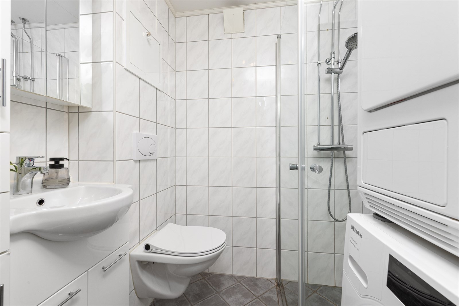 Badet er utstyrt med dusjhjørne, vegghengt toalett, opplegg for vaskemaskin/tørketrommel samt en lys og pen baderomsinnredning. Galleribilde