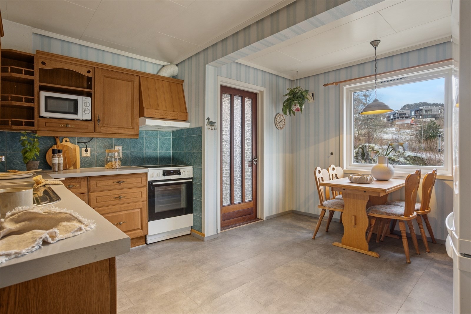 Lyst kjøkken med god arbeidsflate og egen spiseplass ved vinduet - et hyggelig område for hverdagens måltider. Galleribilde