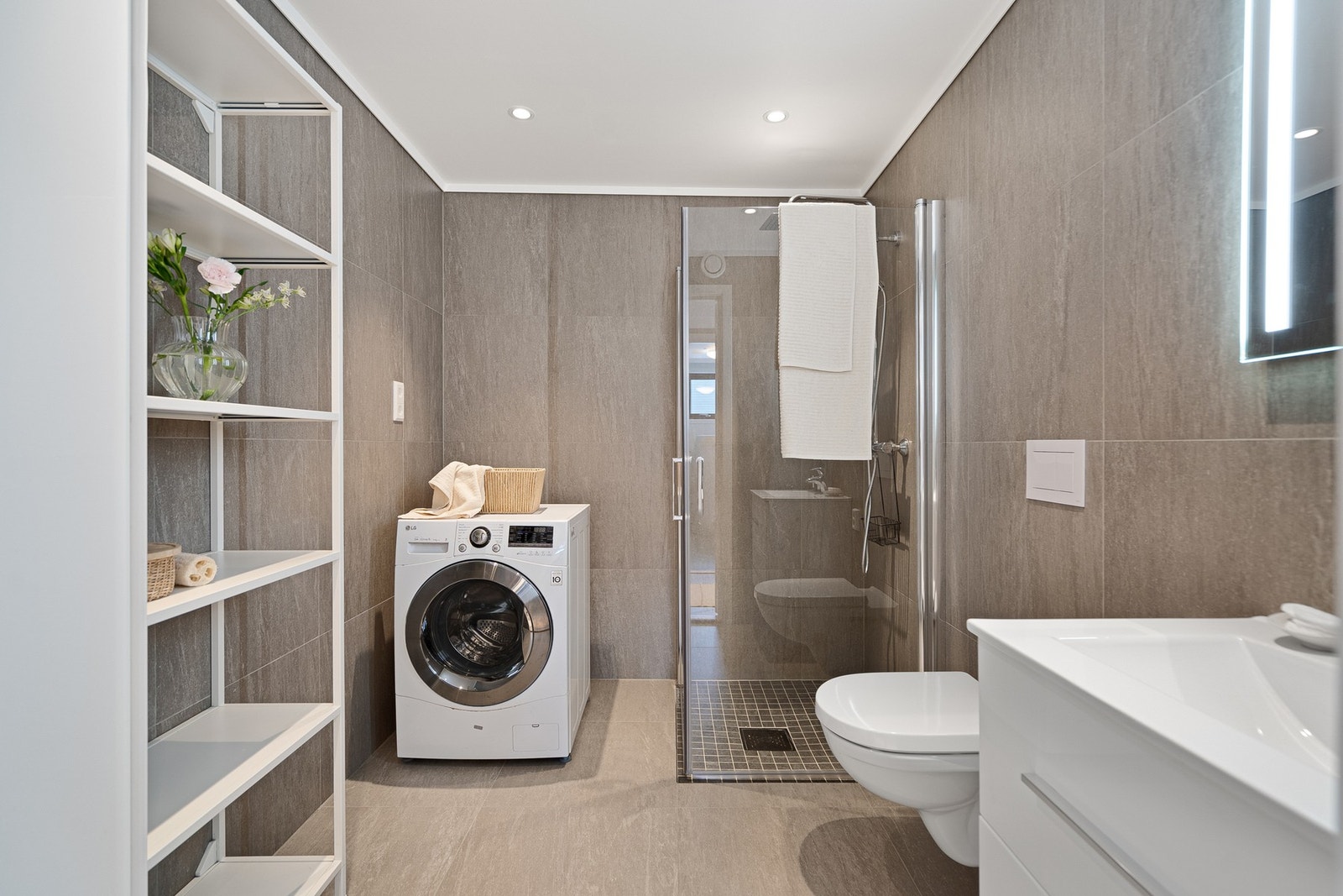 Pent og moderne bad med flislagte overflater. Badet er utstyrt med servant med underskap, toalett og dusjløsning. Galleribilde