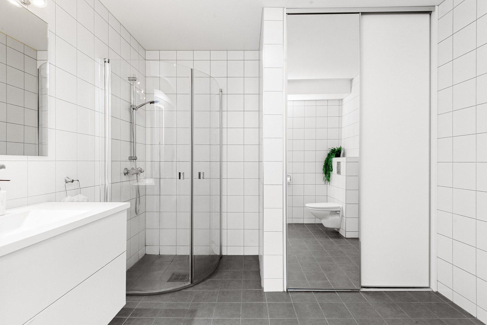 Flislagt bad med opplegg for vaskemaskin bak praktisk nisje med skyvedører Galleribilde