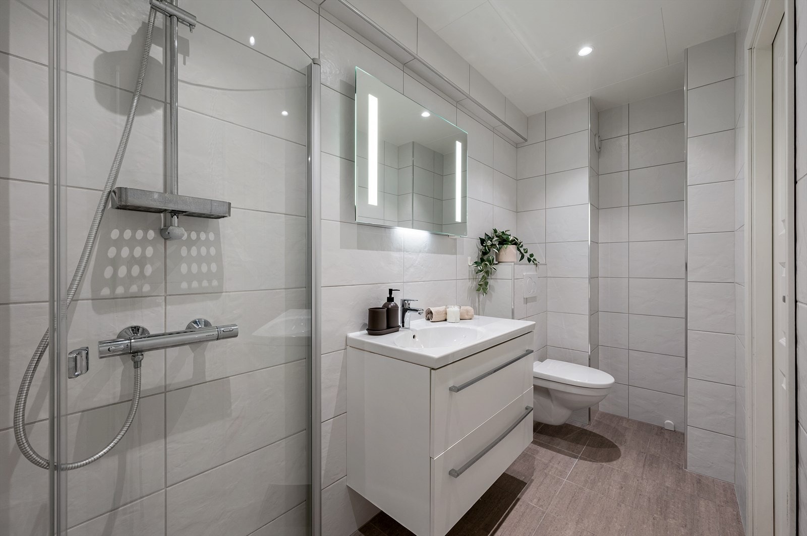 - Badet er innredet med vegghengt toalett, heldekkende servant, speil med belysning og dusjhjørne - Galleribilde