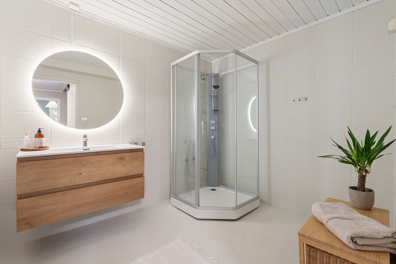 Stort og delikat bad med lyse flater og moderne innredning. Rommet byr på en praktisk dusjløsning, stilren baderomsinnredning med god oppbevaringsplass og et elegant speil med integrert belysning som gir en eksklusiv følelse. Innredning/ dusj fra 2024 Galleribilde